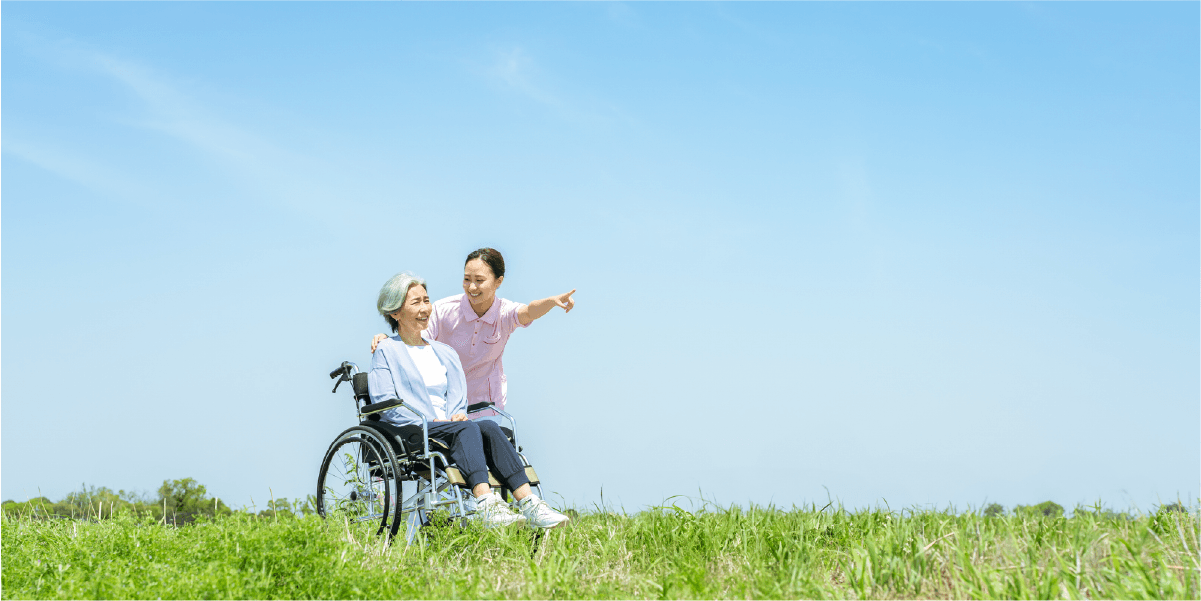 青空の下で車椅子に乗る年配の女性と職員の女性