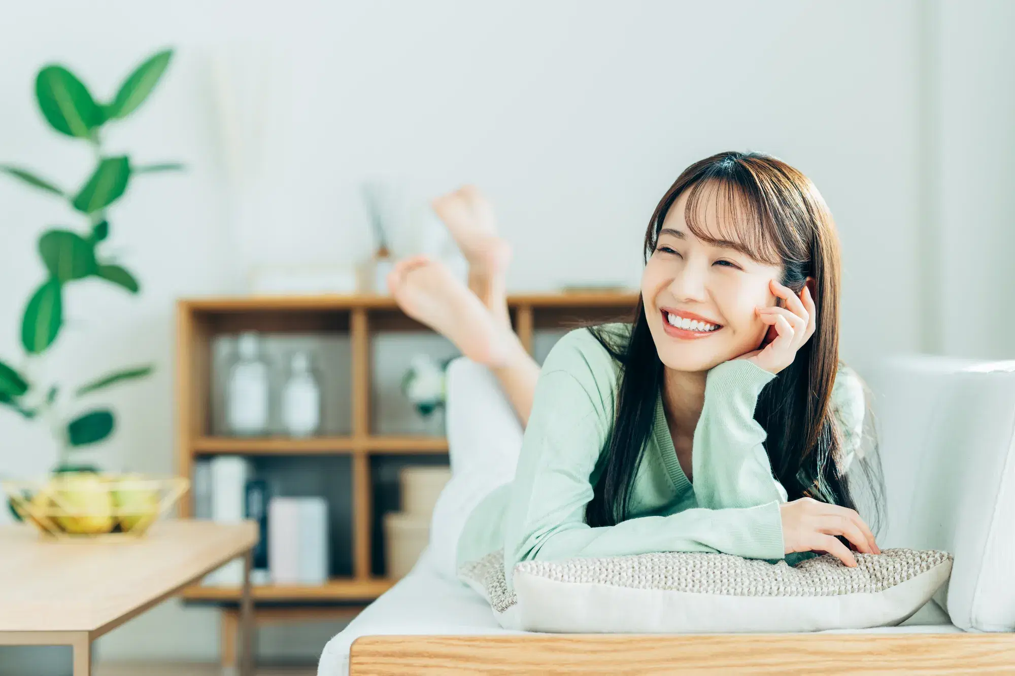 ミントグリーンの服を着た女性がソファにうつぶせに寝転がっている。