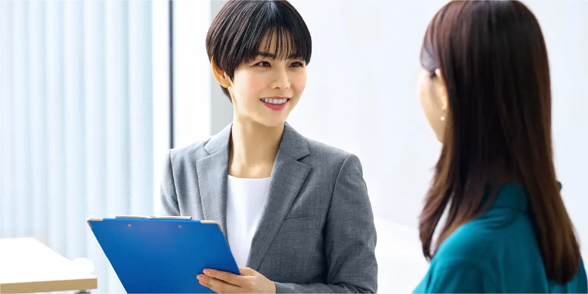 青いバインダーを持ち笑顔で話を聞くショートカットの女性