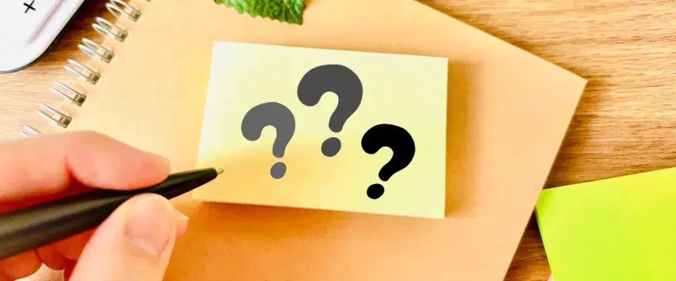 茶色のノートの上に黄色の付箋に書かれている3つの黒い?