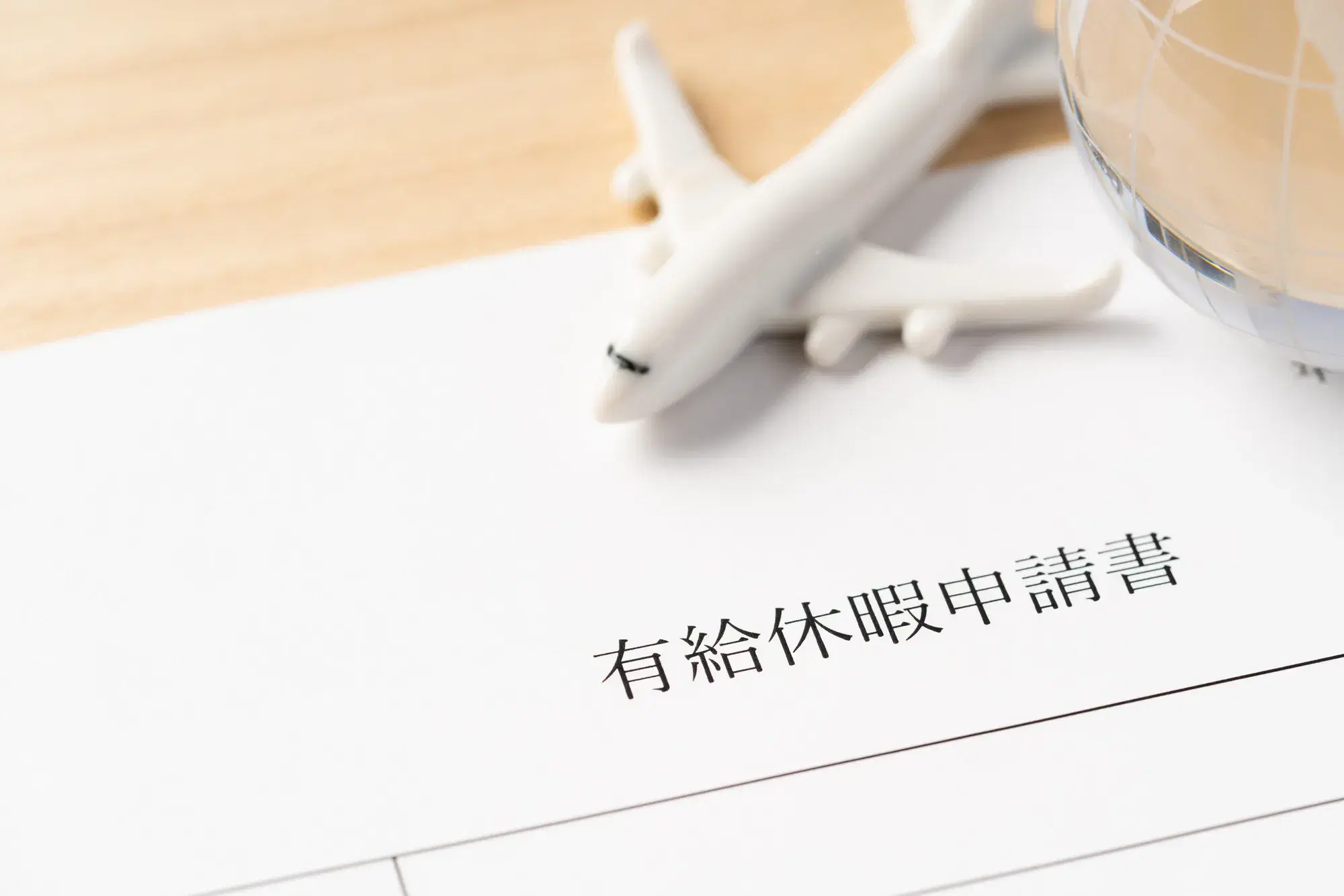 「有給休暇申請書」と書かれた用紙の上に、飛行機の模型と地球儀が置かれている様子が写っている。
