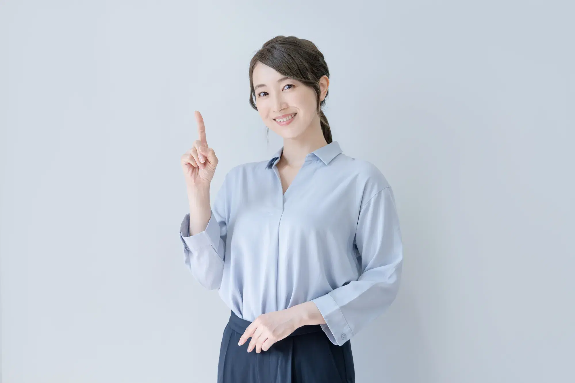 水色のシャツに紺色のスカートをはいた女性が人差し指を立てている