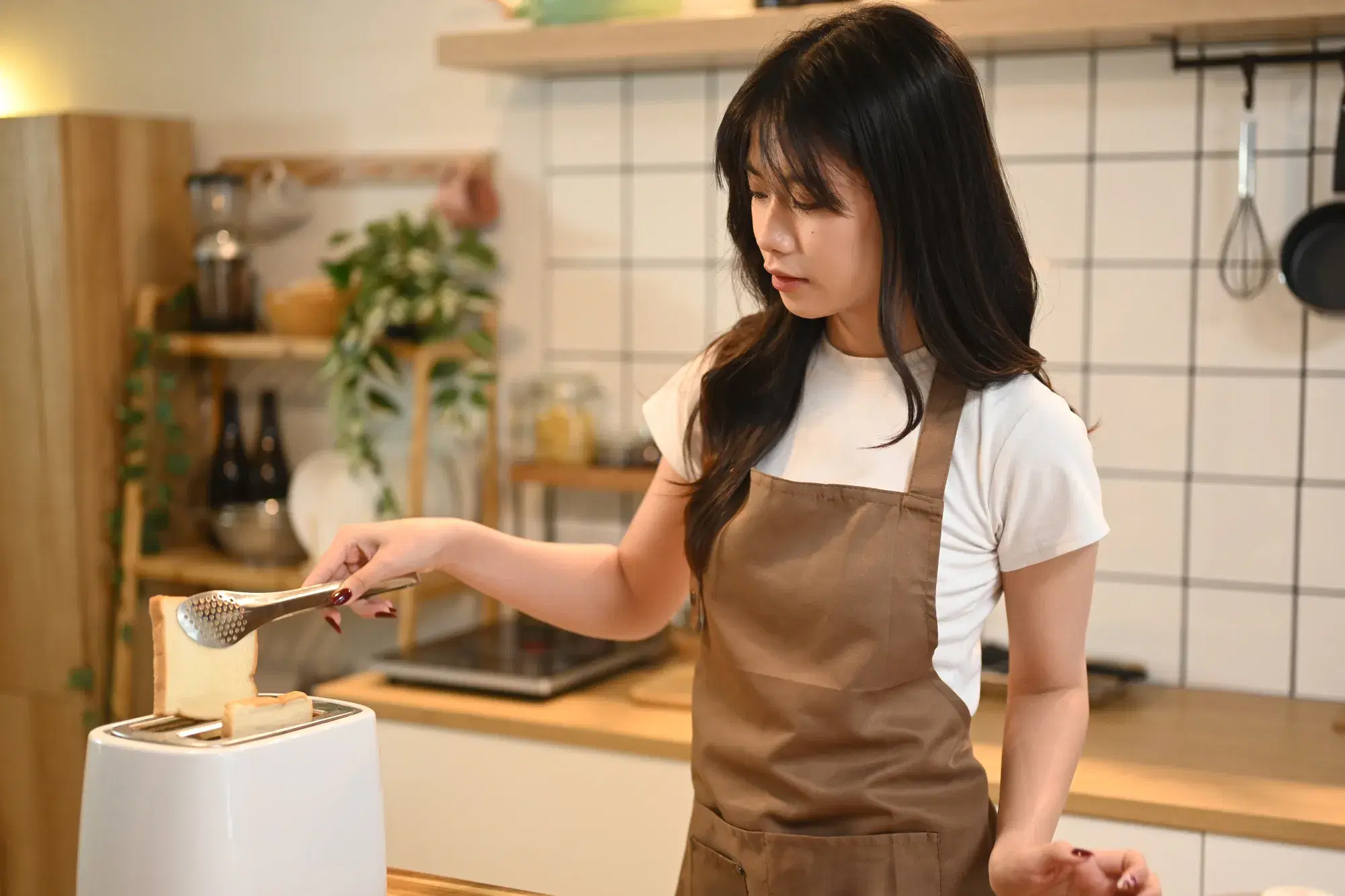 茶色のエプロンを着用した女性がトングで食パンを掴む