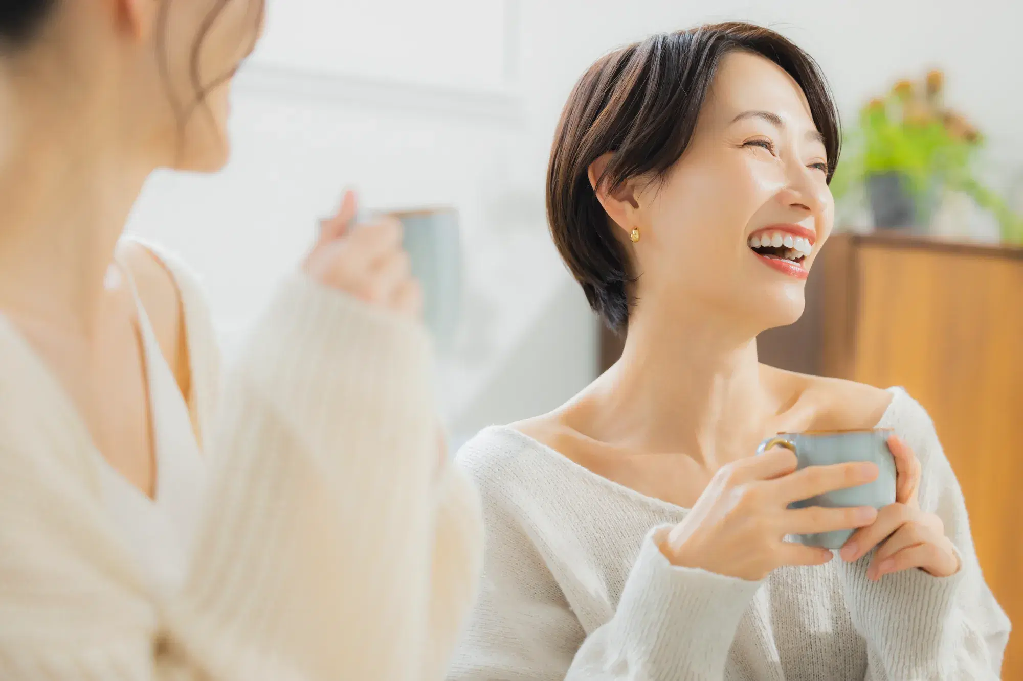 複数の人数と一緒に笑顔で会話をしている両手でカップをもった灰色の服を着た女性