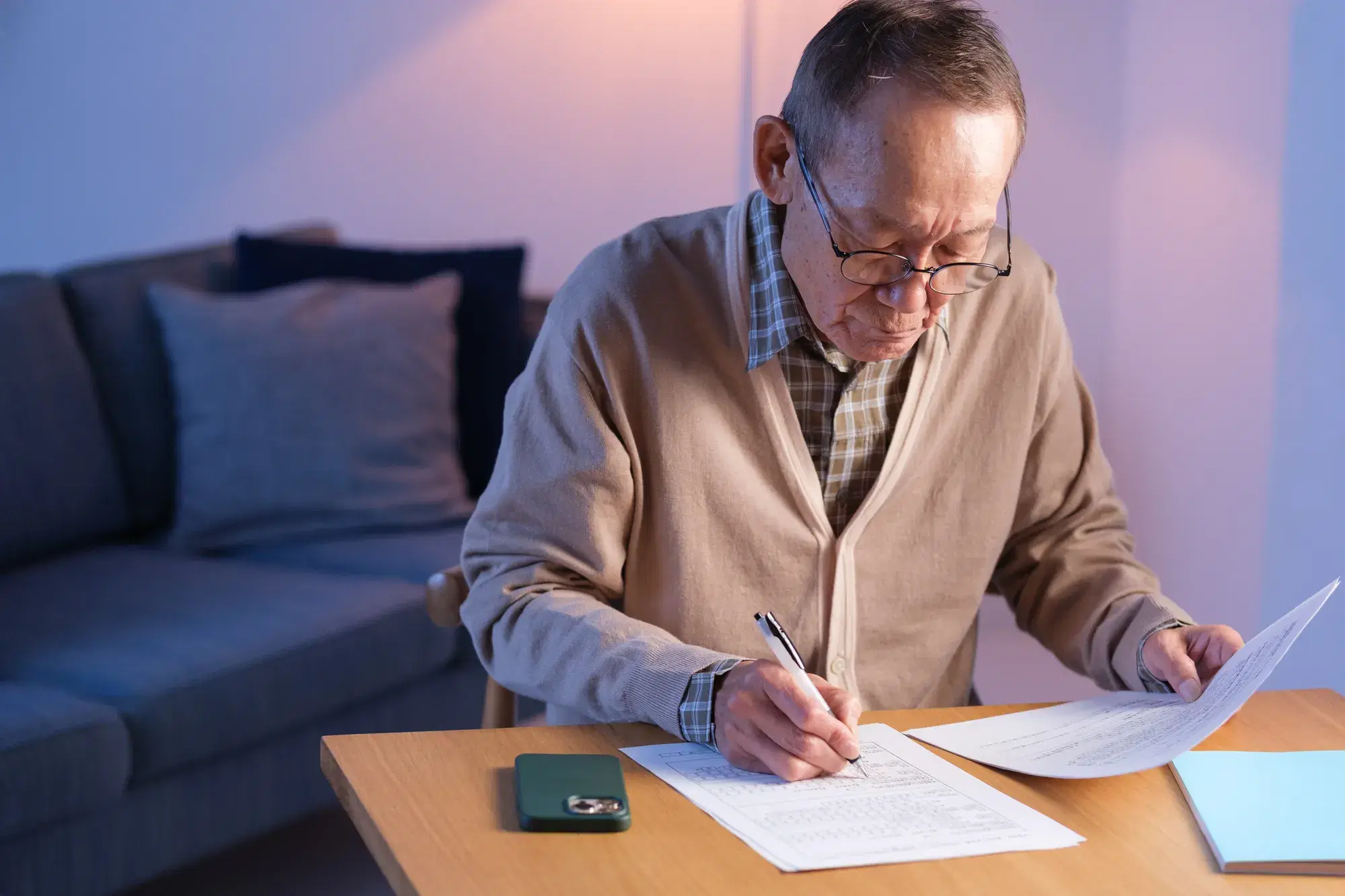 茶色の服を着た男性がソファのある部屋で机に向かって勉強している。