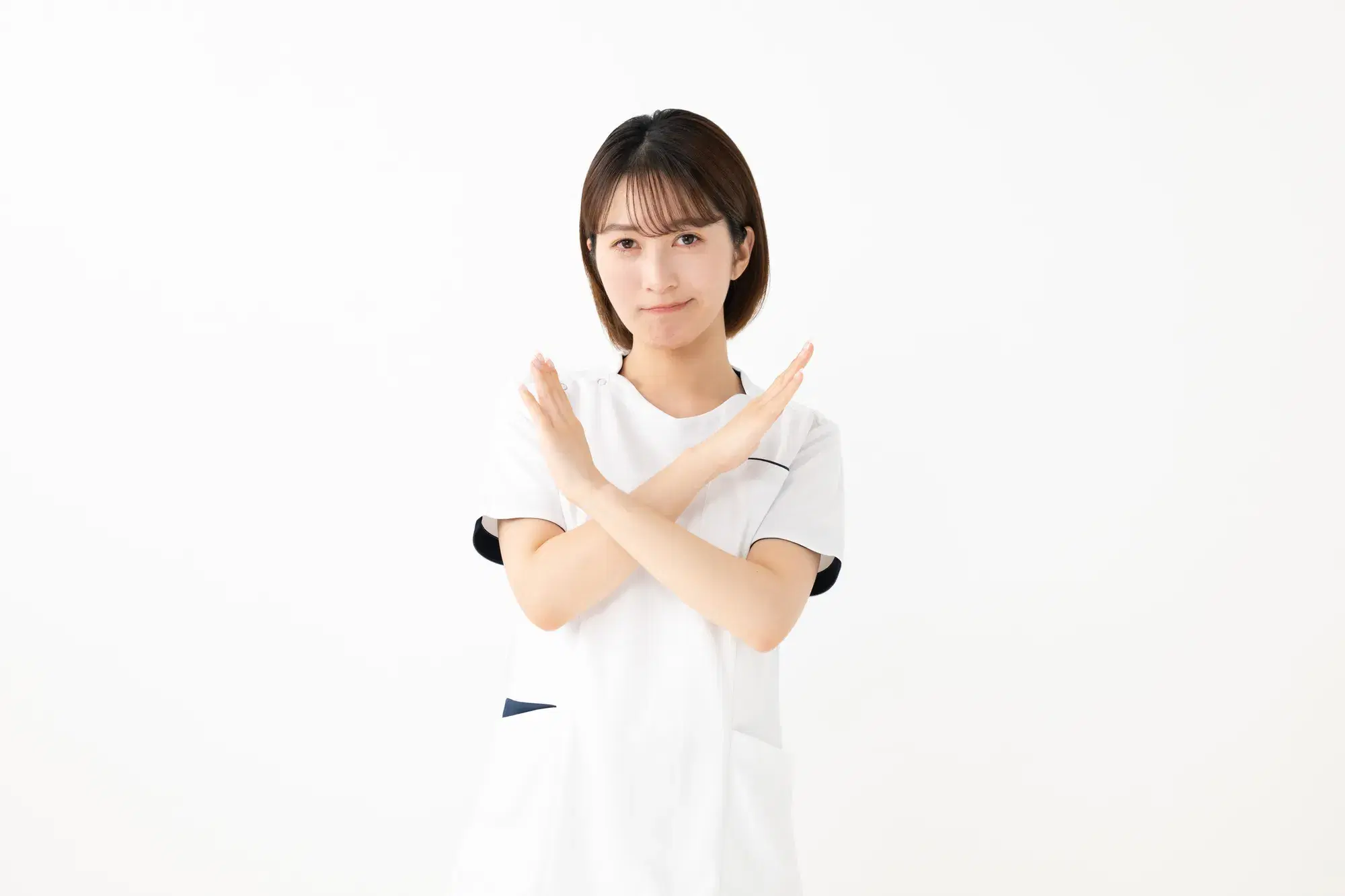 白い服を着た女性の医療従事者が、胸の前で腕を交差させてバツ印を作っている。