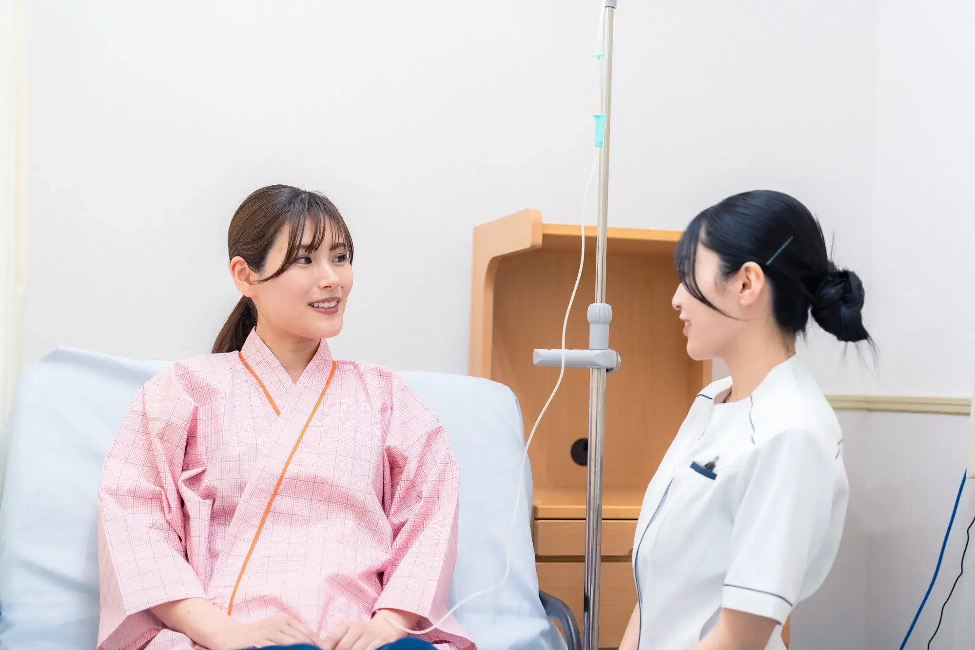 ピンク色の服を着た患者がベッドに上半身を起こした状態で座っており、看護婦と話している。