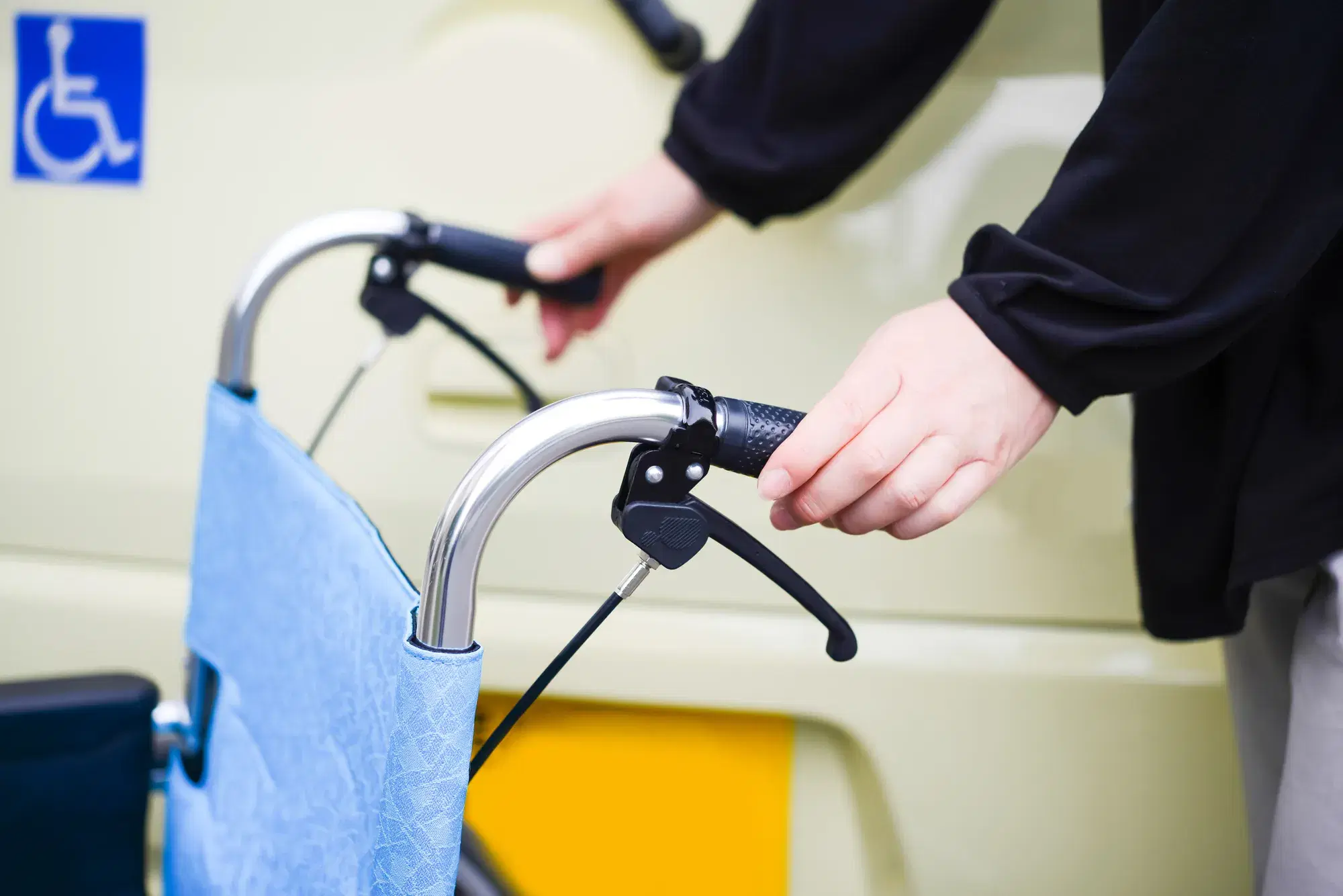 黒い服を着た人が水色の車いすを握っている。