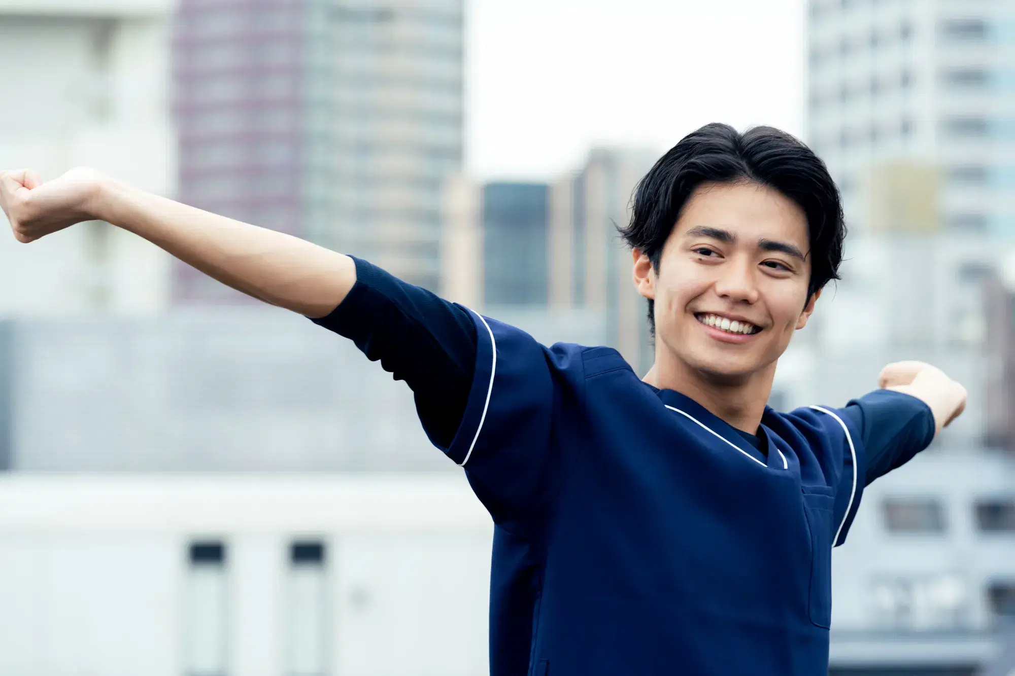 紺色のスクラブと黒いインナーを着た男性が両腕を伸ばしてストレッチをしている。