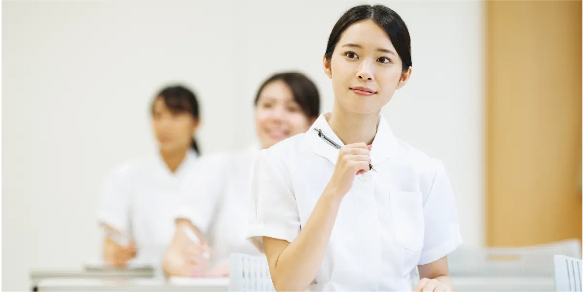 女性が三人並んでいる。一番前の女性はペンを持って首を傾げている。