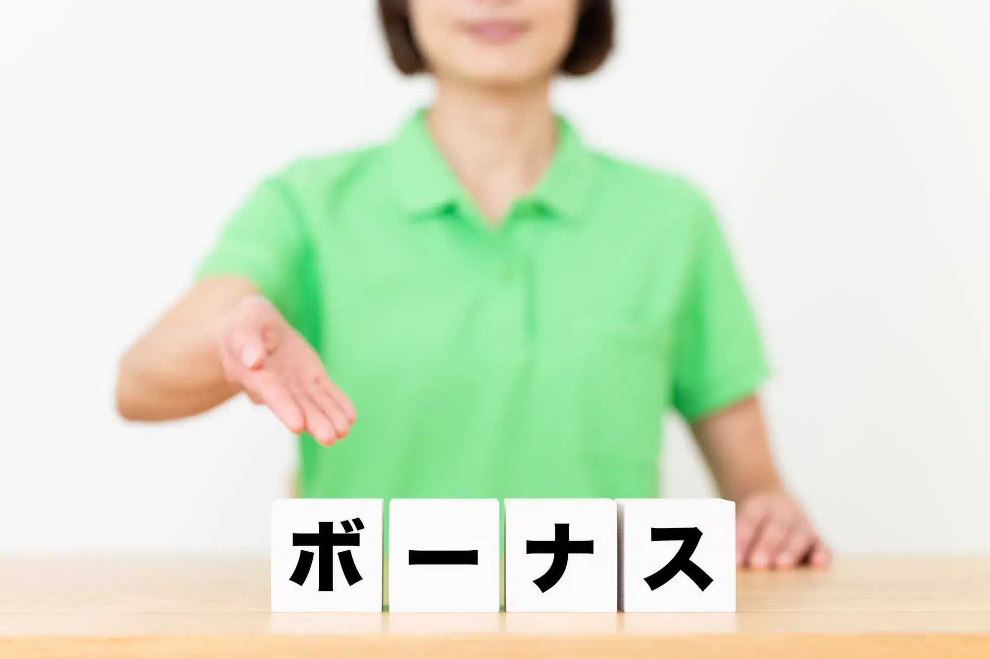 緑の服を着た女性がボーナスと書かれた白いブロックを手で指す