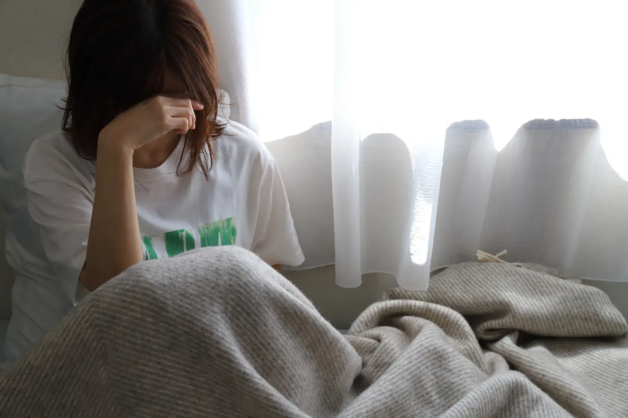 白いカーテンの前で白いシャツを着た女性が頭に手を添えている