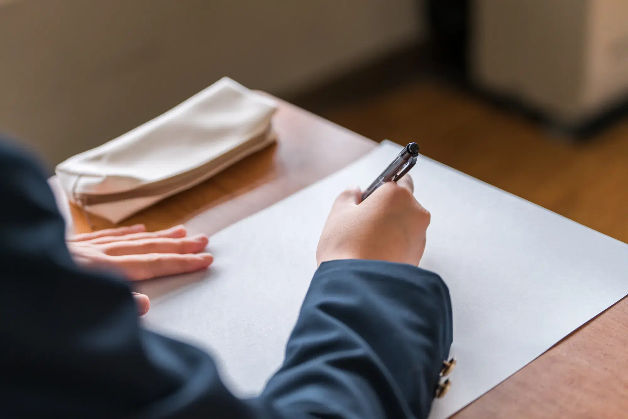 黒い服を着た人が机に座り白い紙に文字を書こうとしている
