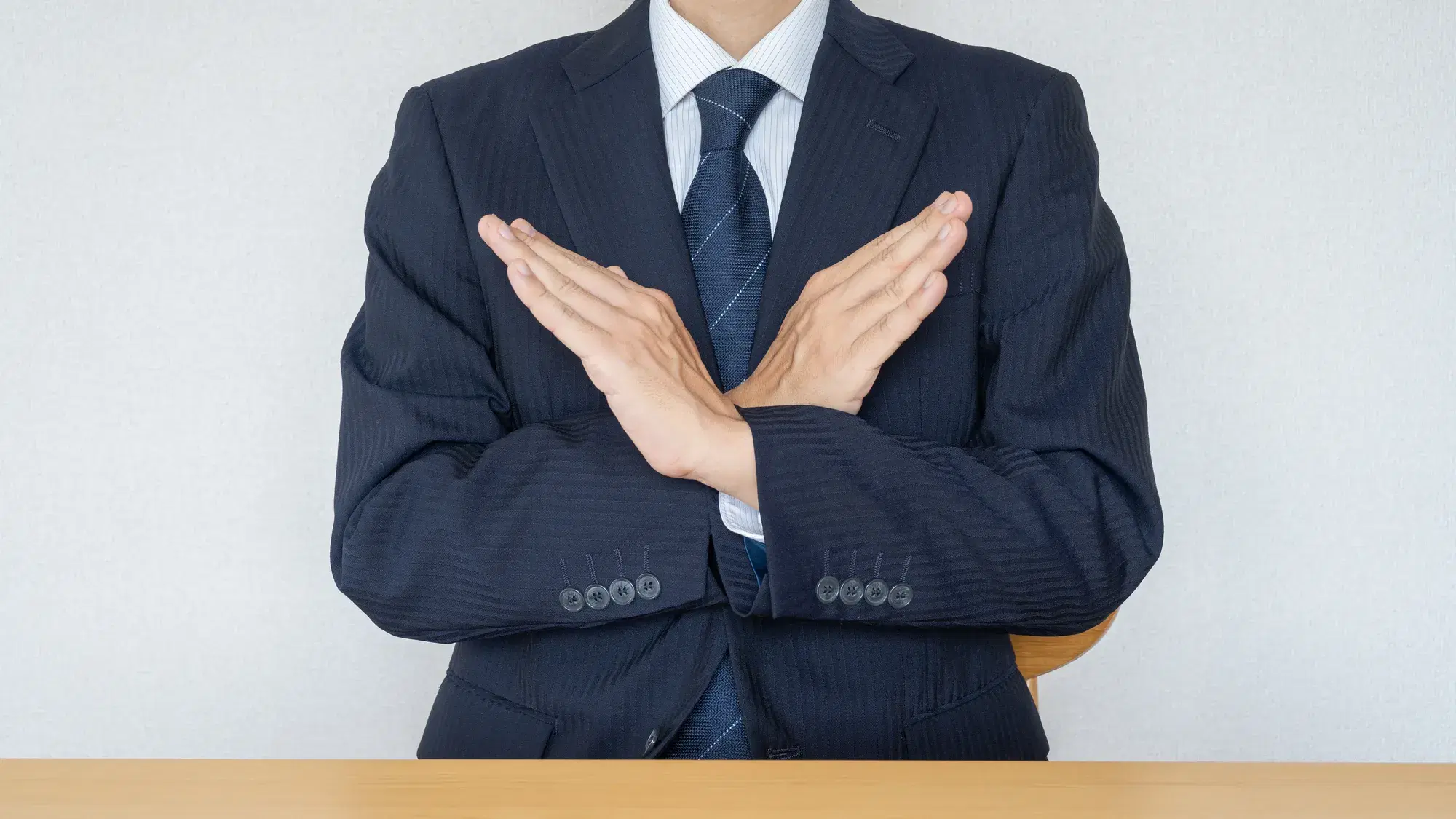 スーツの男性が胸の前で腕を交差させバツ印を作っている