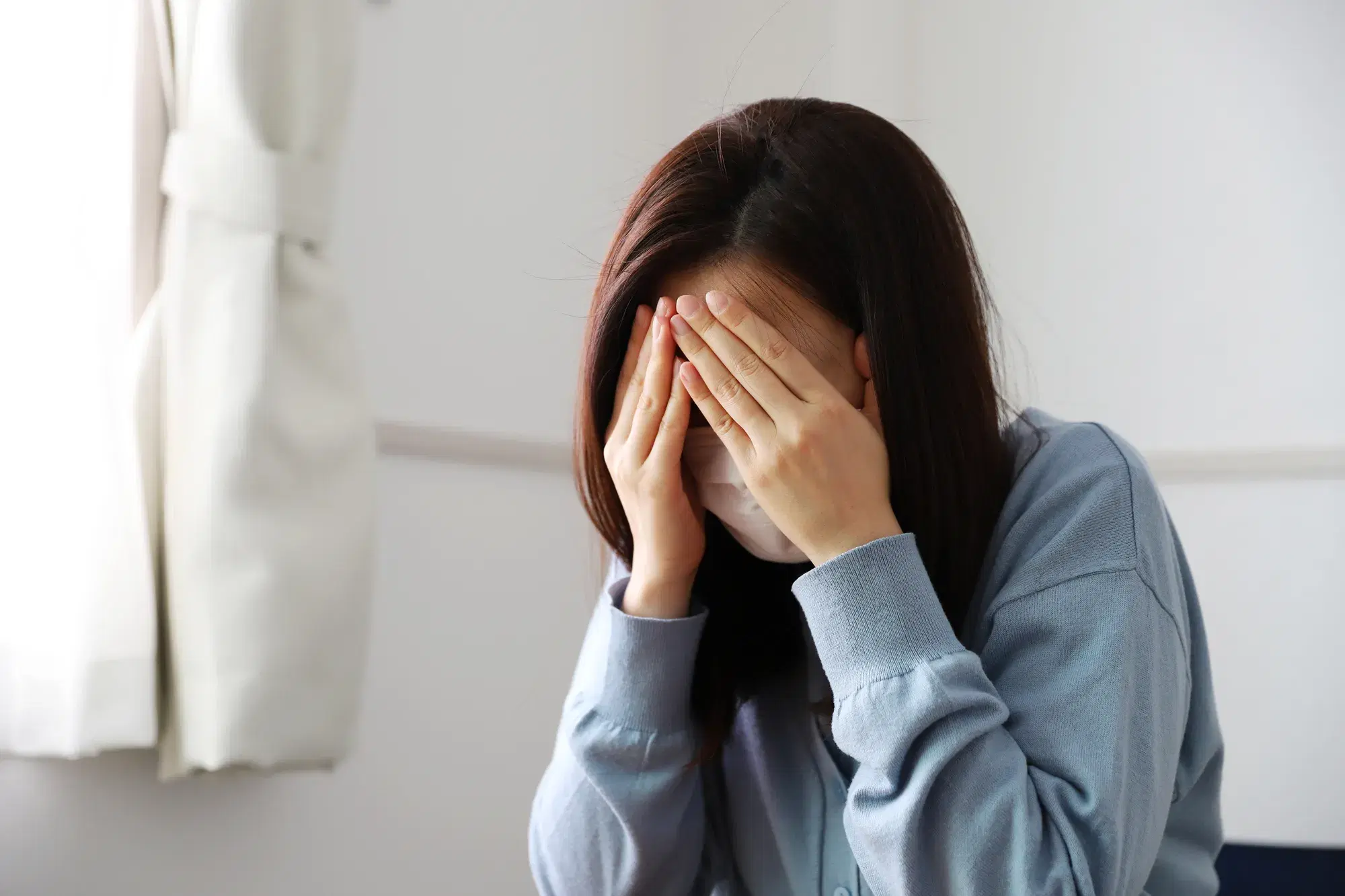 手で顔を覆っている青い服を着たマスクをした女性