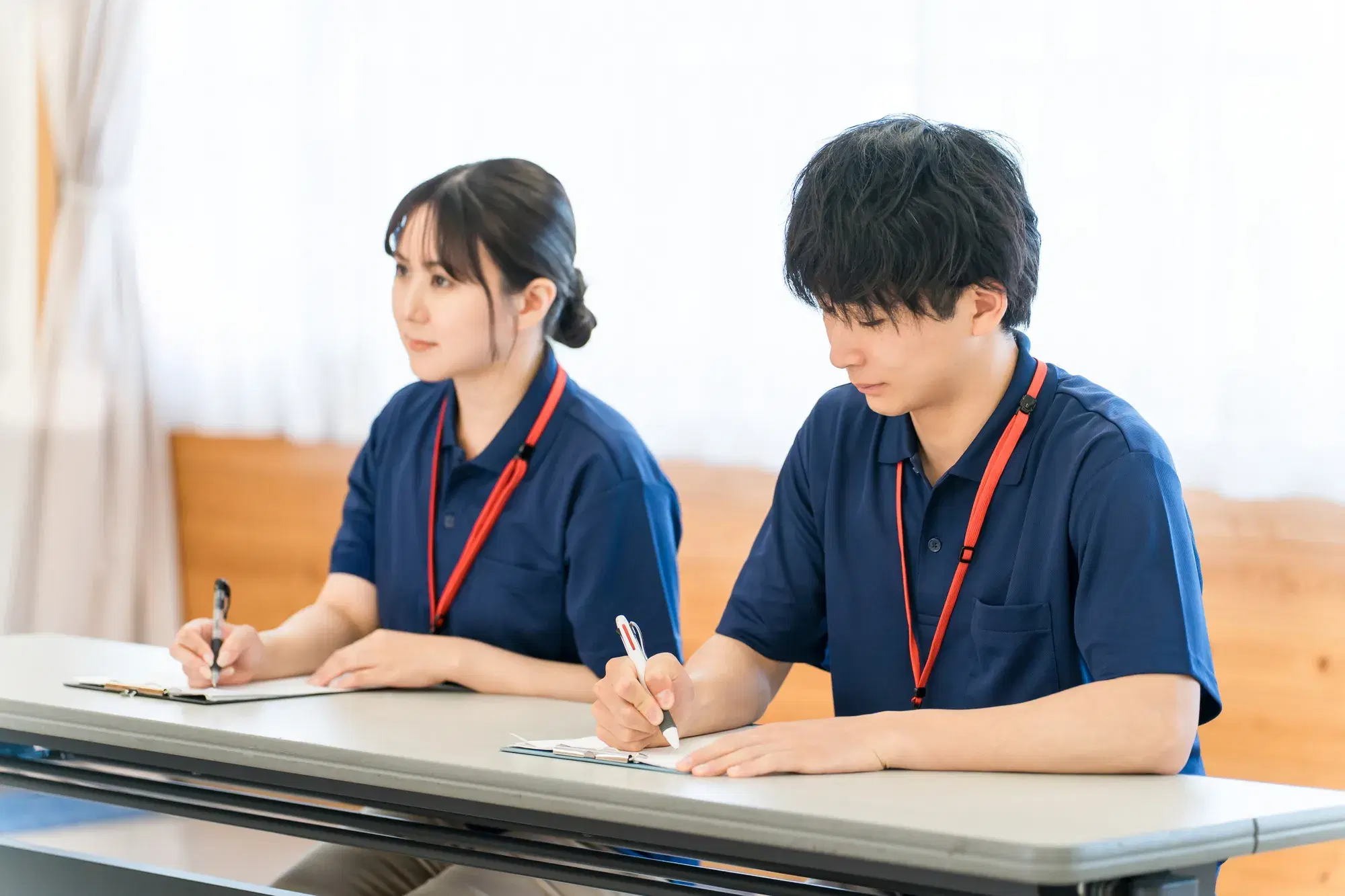 首から赤色のストラップを下げている青色の服を着た男女がメモ