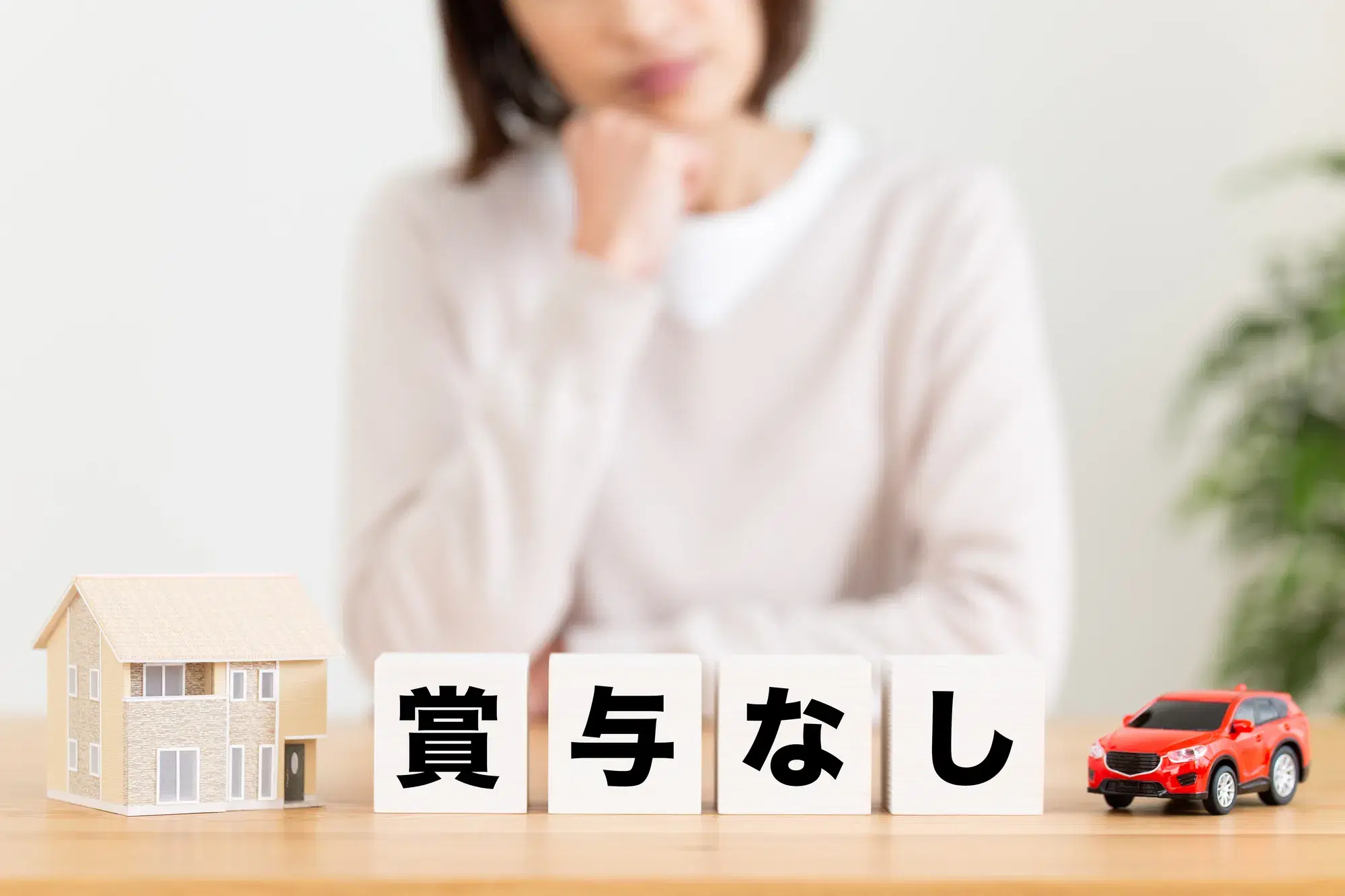 賞与なしと書かれている白いブロックが乗っているテーブルと顎に手を当てて考える女性
