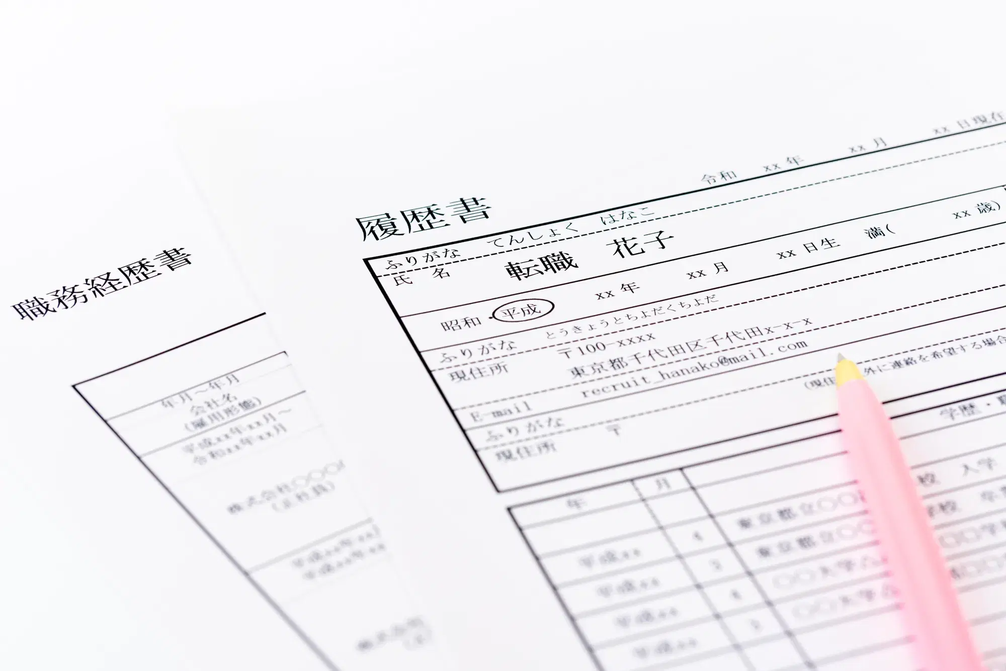 「履歴書」と「職務経歴書」と書かれた用紙の上にピンクのペンが置かれている様子が写っている。