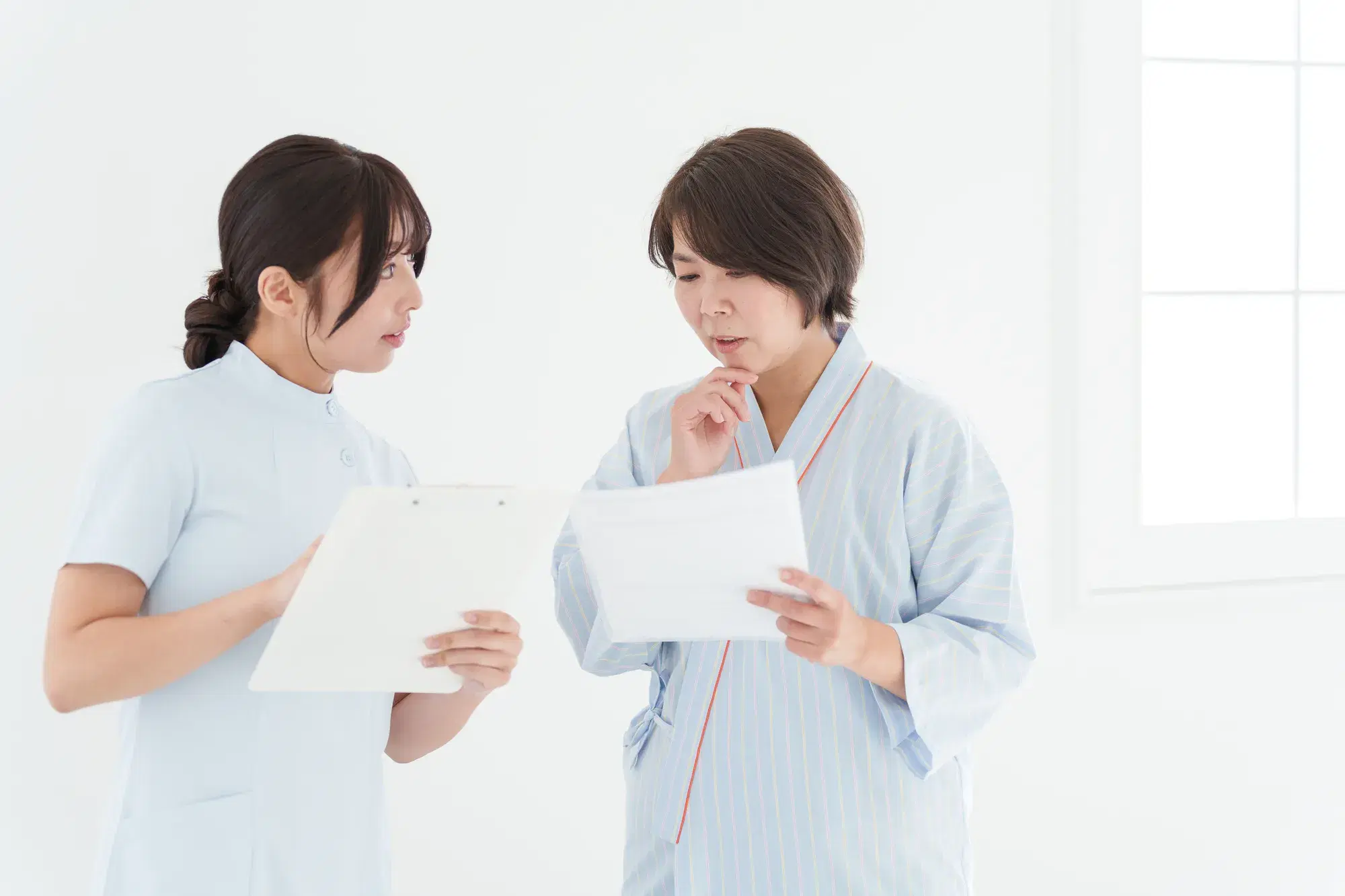 白衣を着た女性と水色の縞模様の服を着た患者が書類を見ながら話し合っている