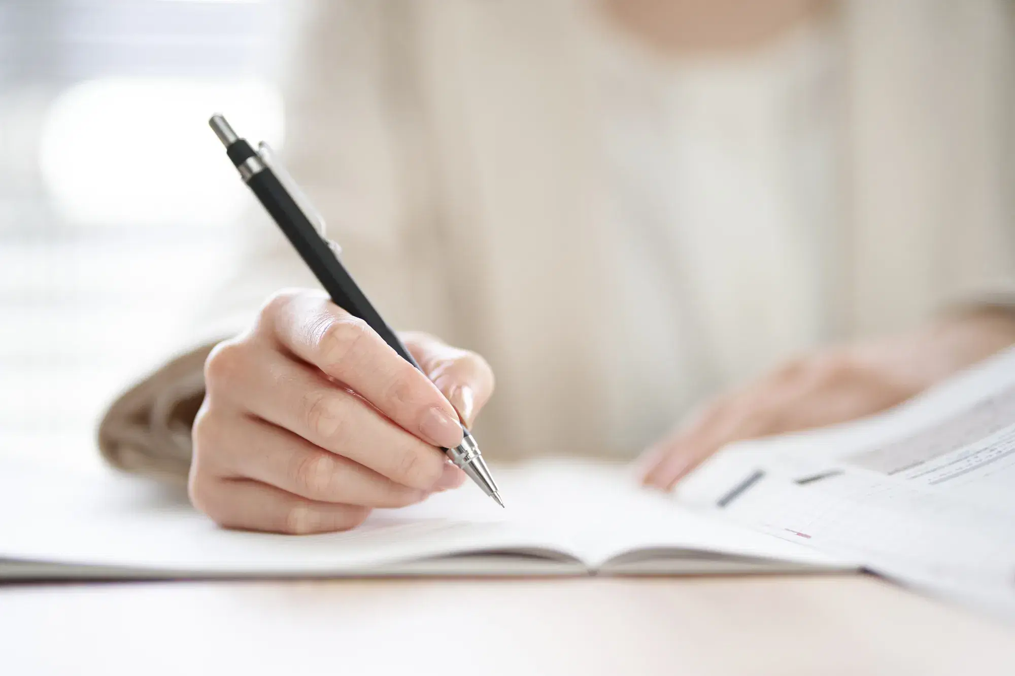 白い服の人がノートにペンで文字を書いている