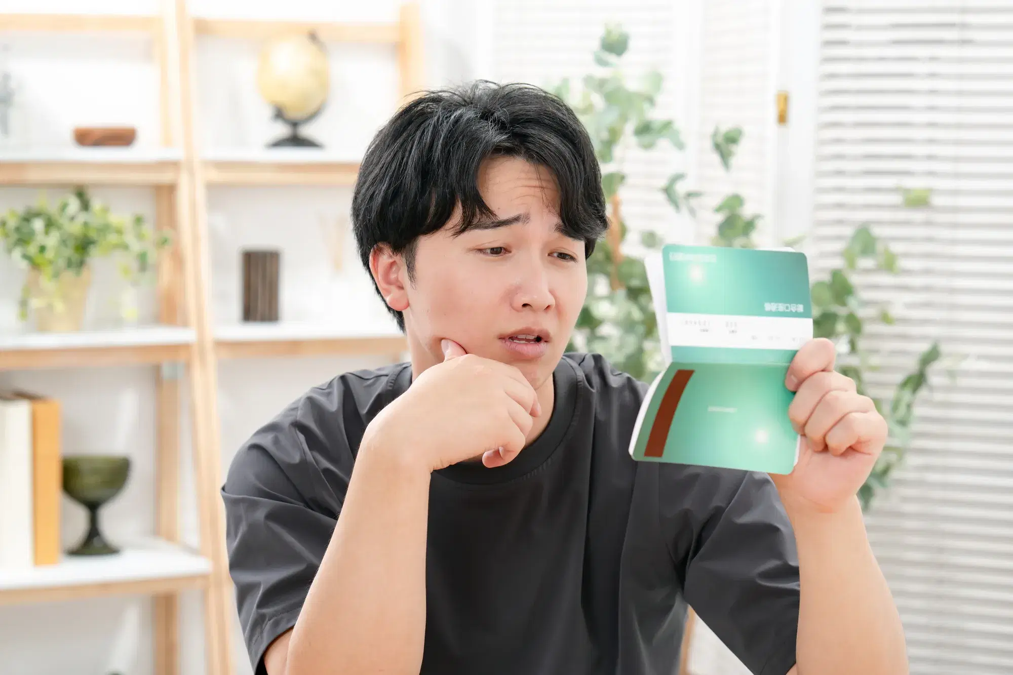 黒い服を着た男性が通帳を片手に顎に手を添えながら悲しい表情