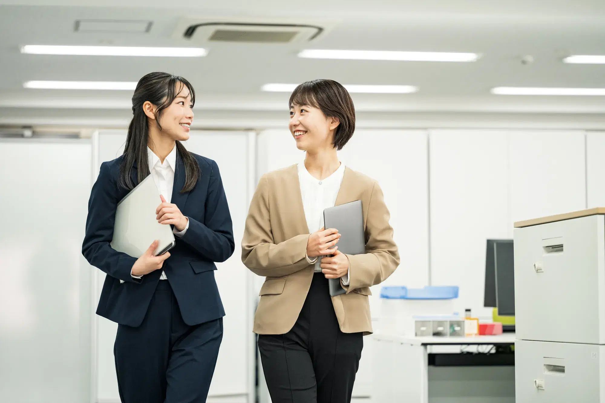 黒いスーツを着た女性とベージュ色のスーツを着た女性が歩きながら会話