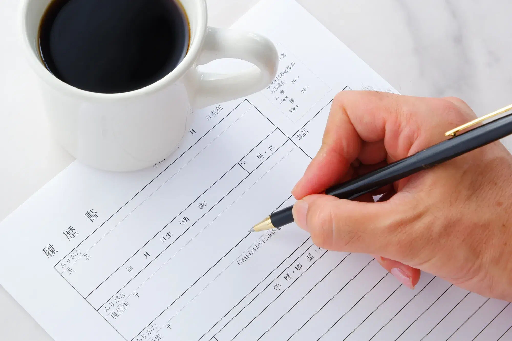 履歴書の上にコーヒーが入ったコップと筆記用具