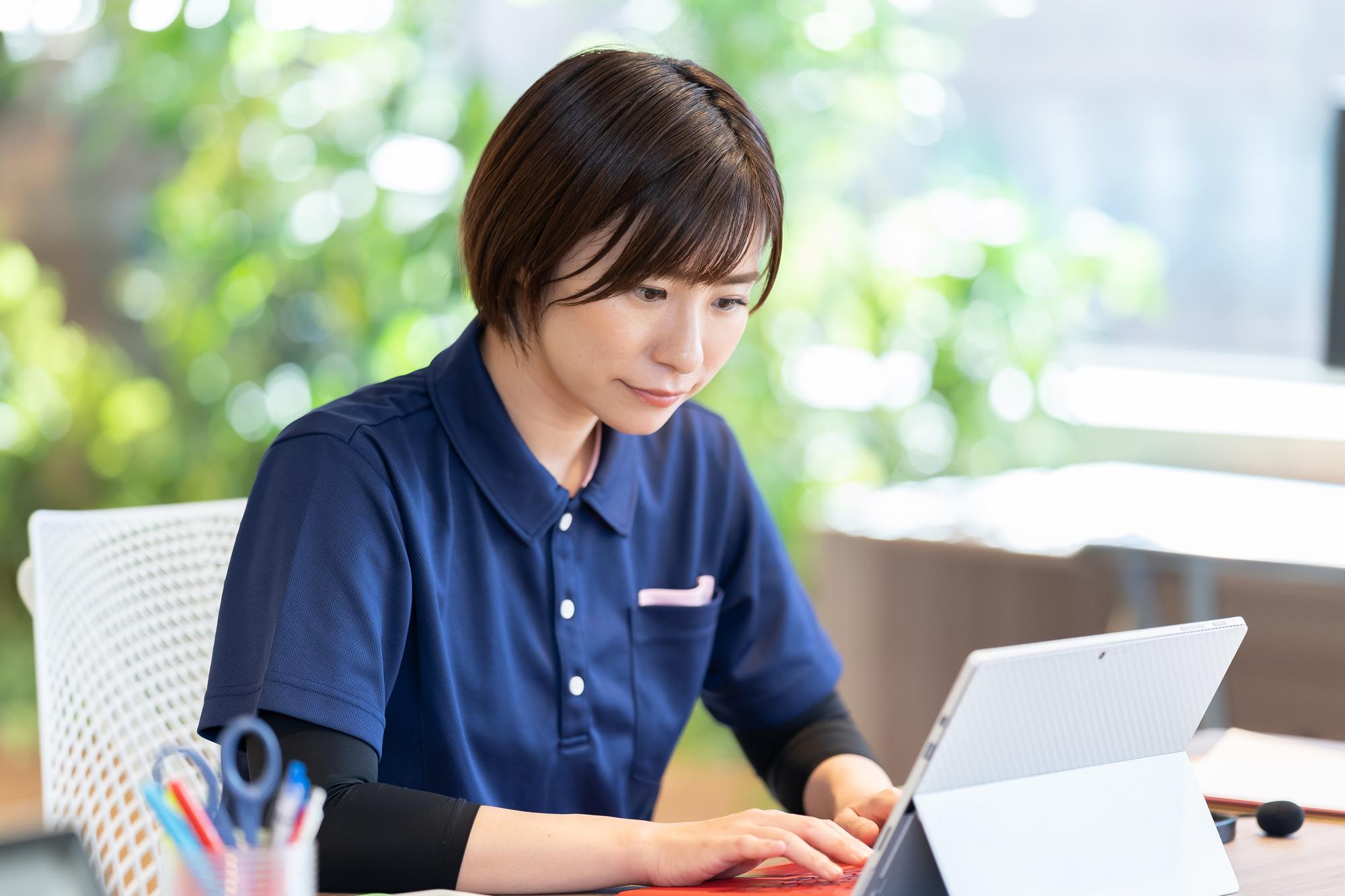 紺色の服を着た医療従事者がタブレットで作業をしている
