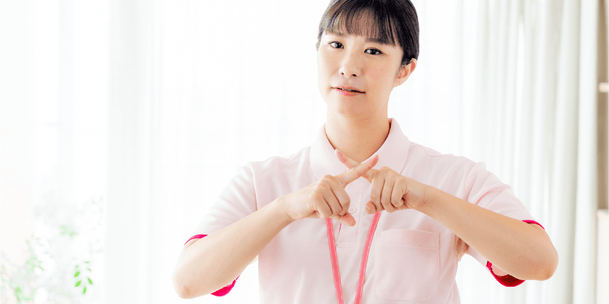 手で×マークを作る介護職員の女性