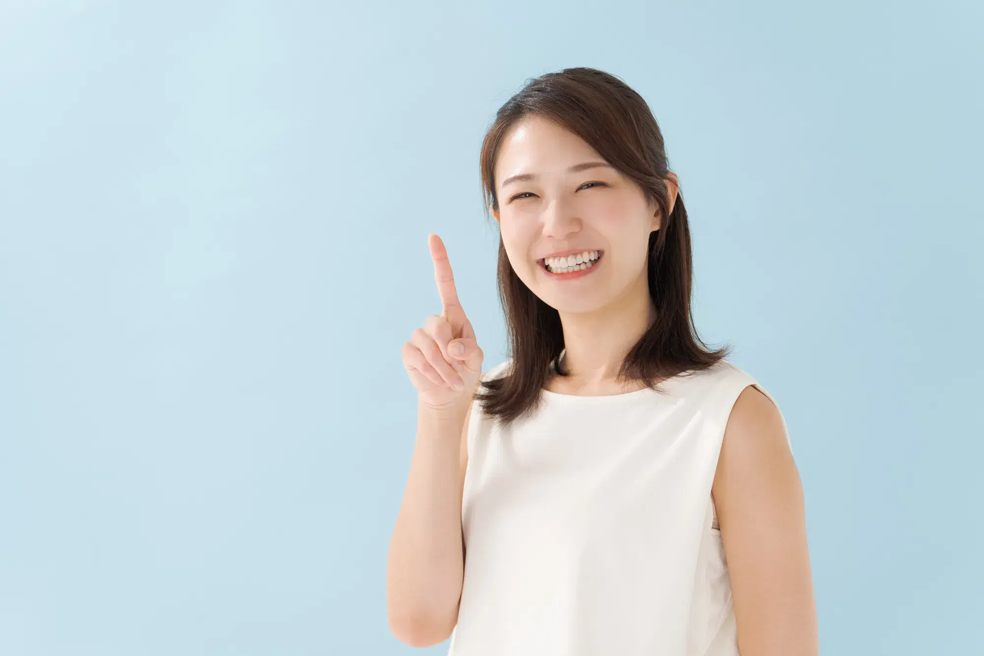 白い服を着た女性が人差し指を1本立てて立っている。