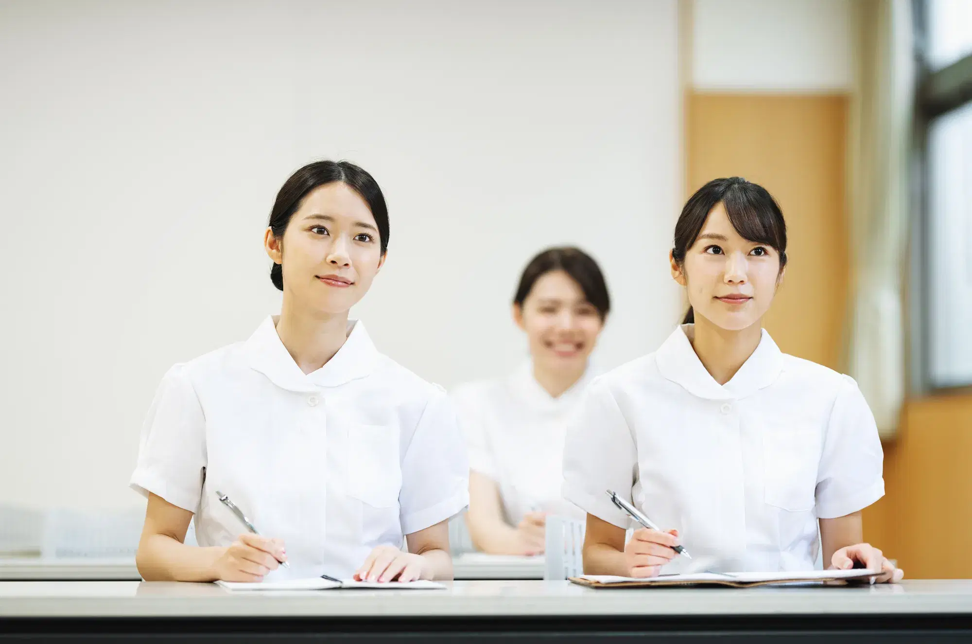 白衣を着た女性たちが講義を聞いている