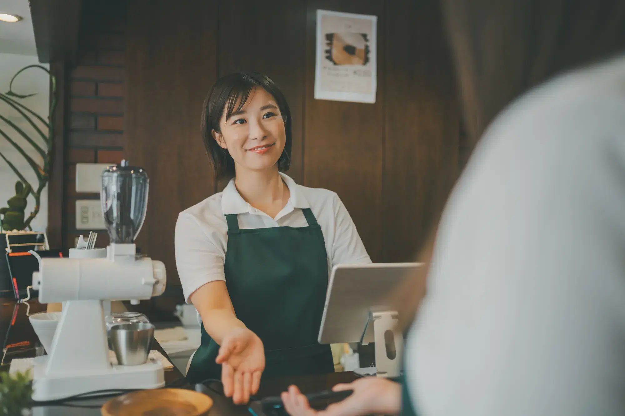 緑のエプロンを着用したカフェの女性店員