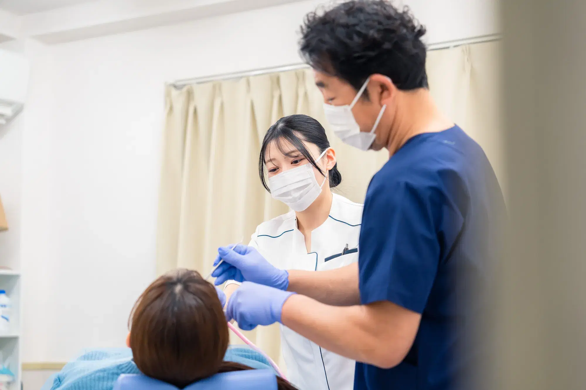 紺色のスクラブを着た男性の医療従事者と白いスクラブを着た女性の医療従事者が、水色の服を着た治療中の人物を処置している。