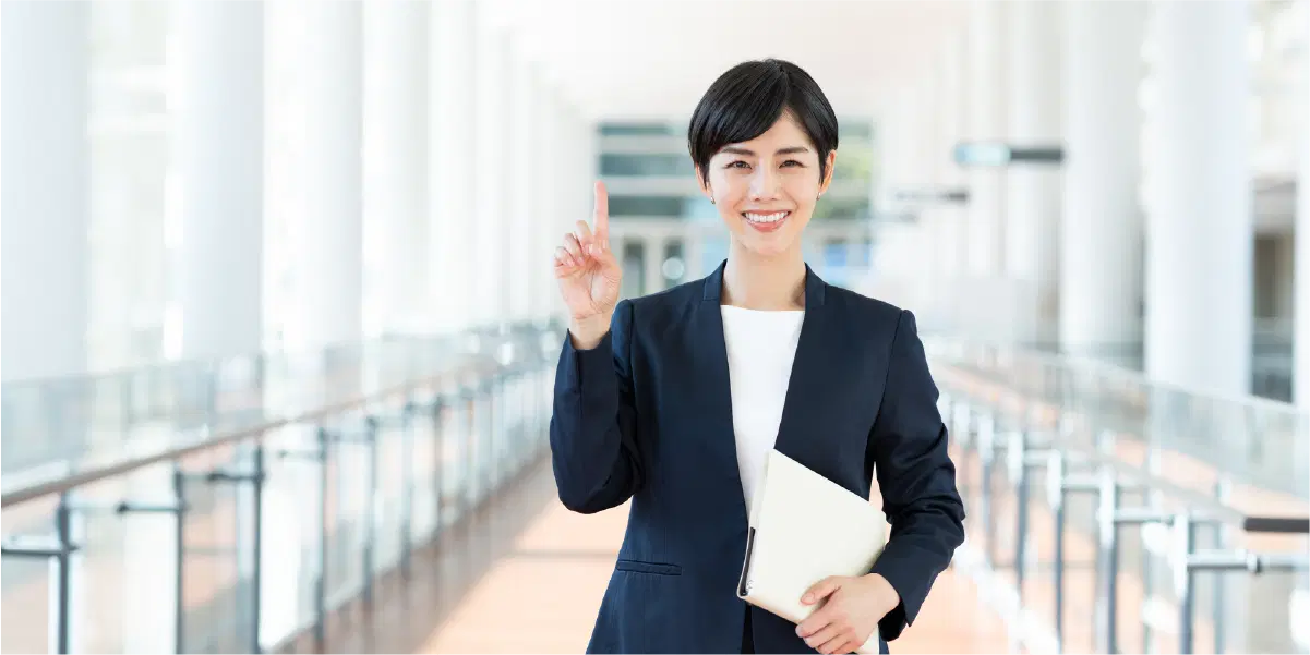 廊下でバインダーを持ち人差し指を立てているスーツの女性