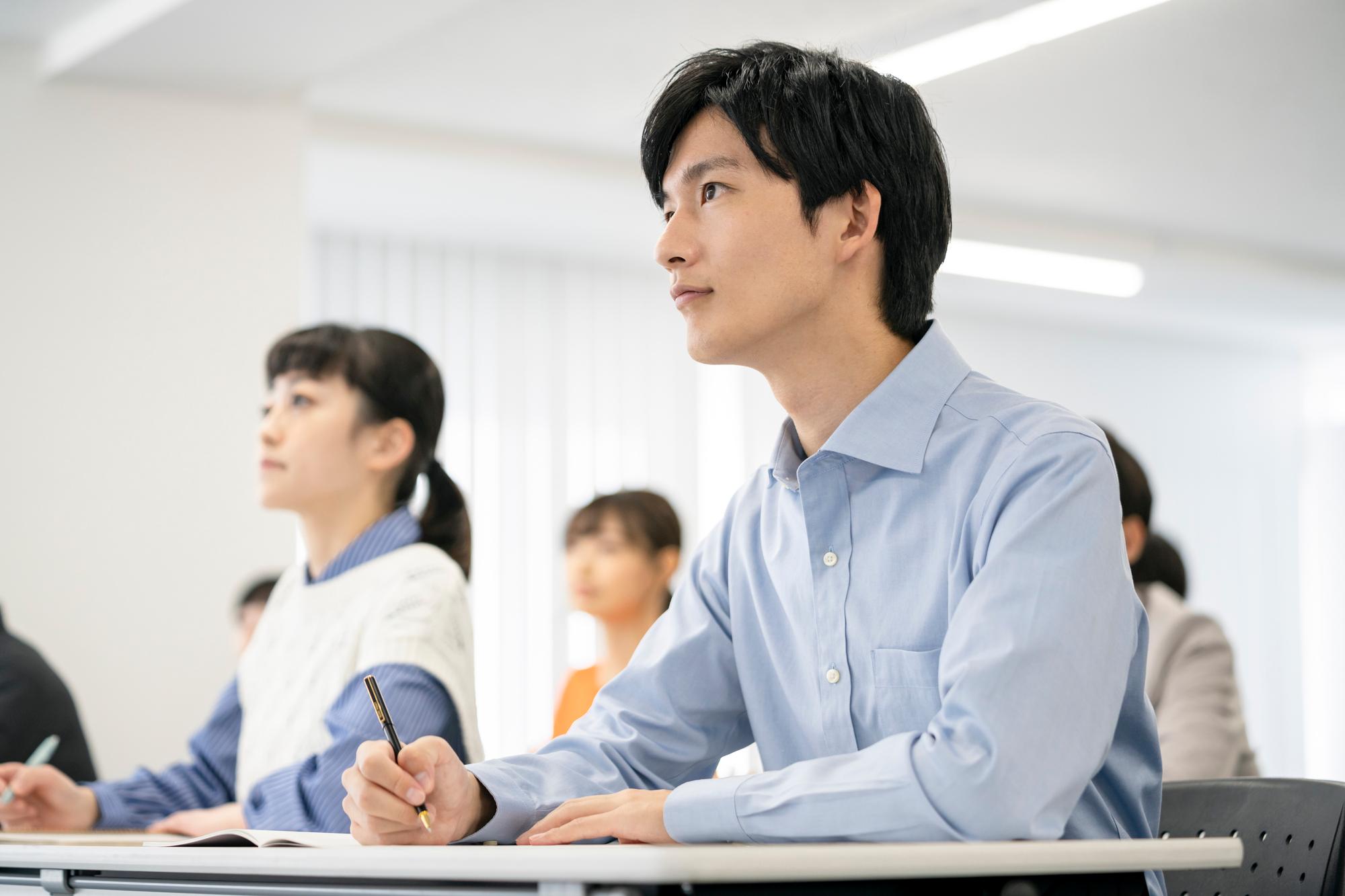 水色の服を着た男性と青い服の上に白いニットを着た女性が講義を聞きながらメモを取っている