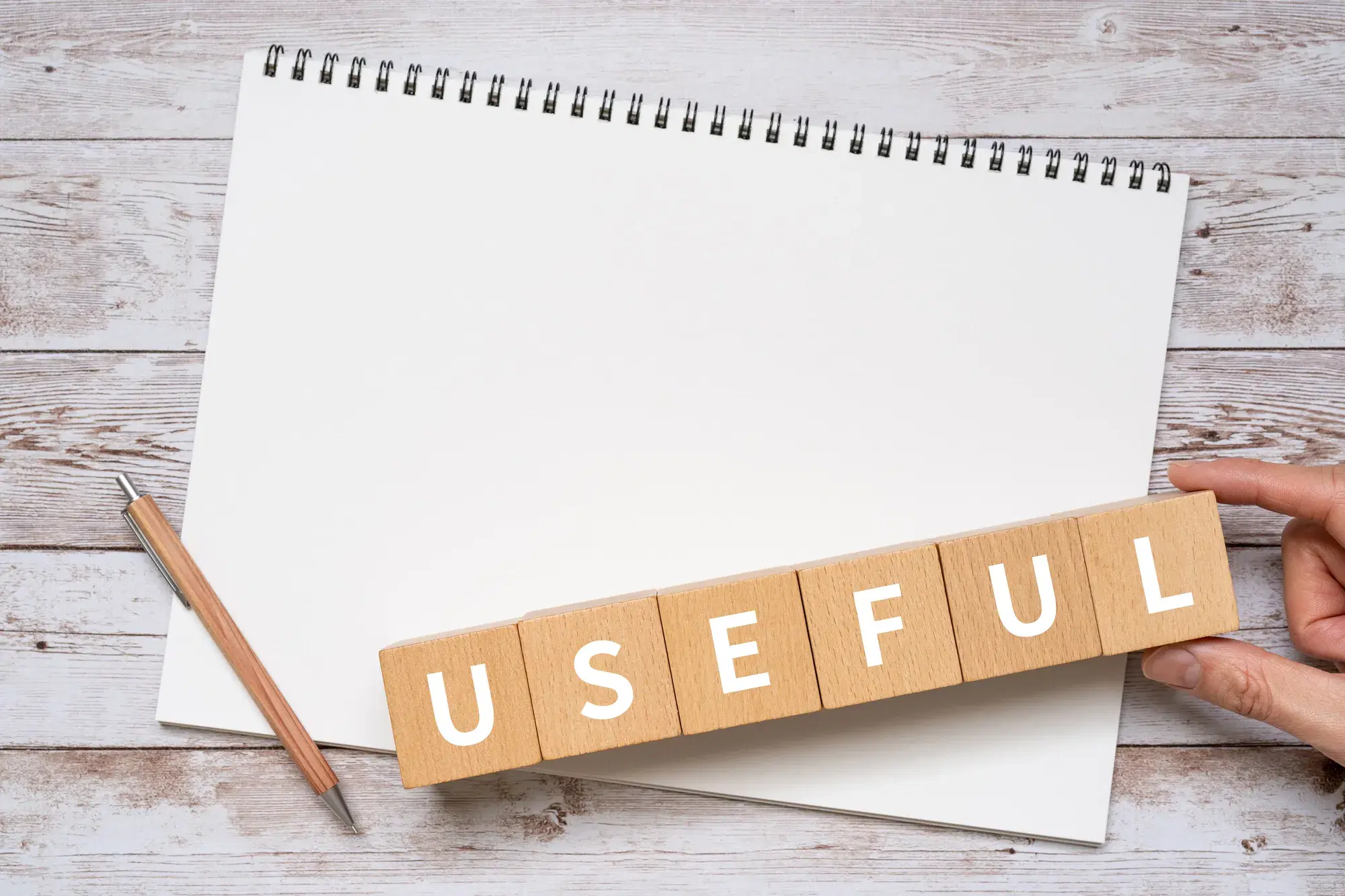 ノートの上にペンとusefulと書かれた積み木が置いてあり、積み木は手で持たれている。