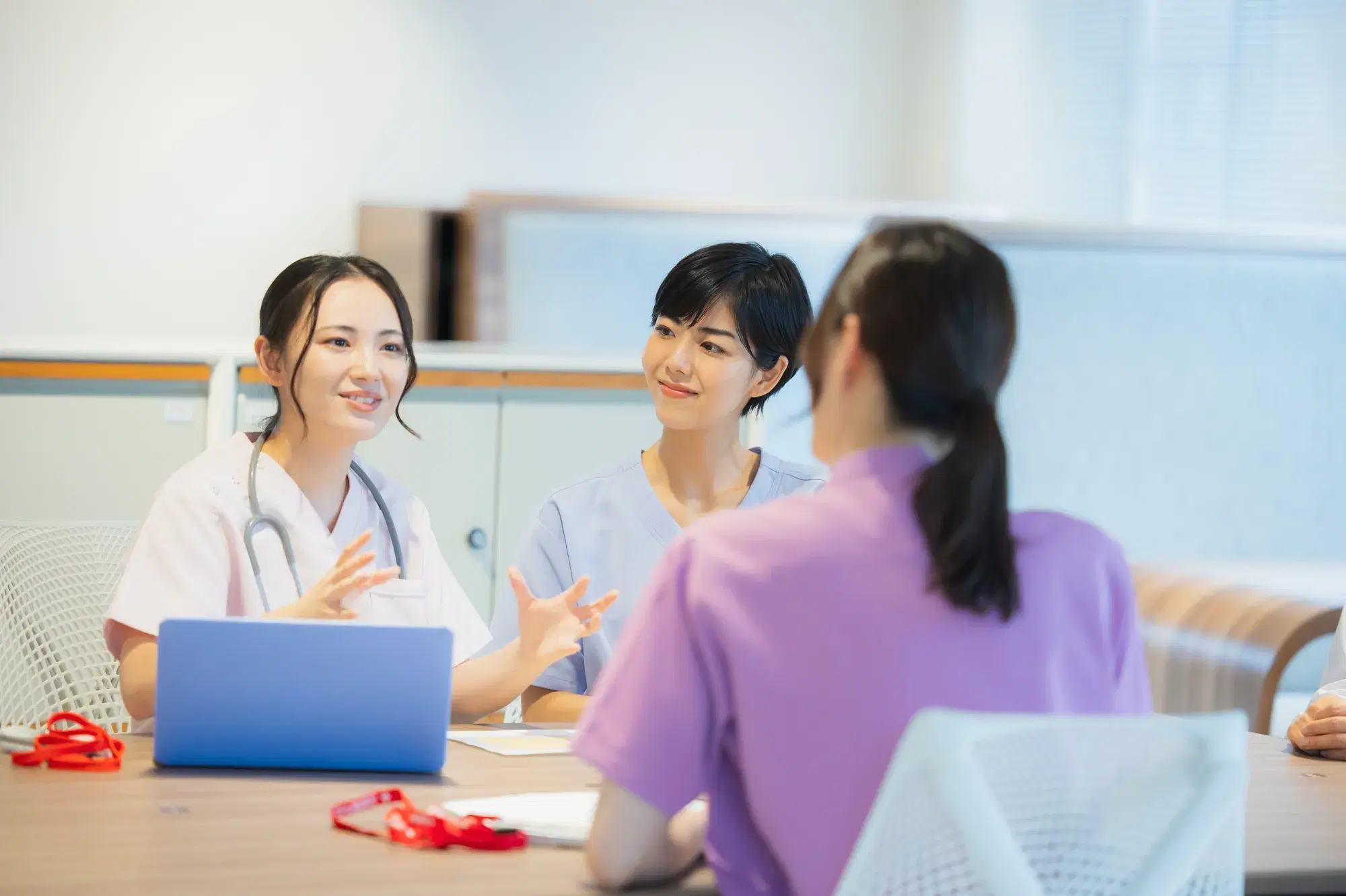 白衣の人間が話しているのを紫の服を着た女性と青の服を着た女性が聞いている