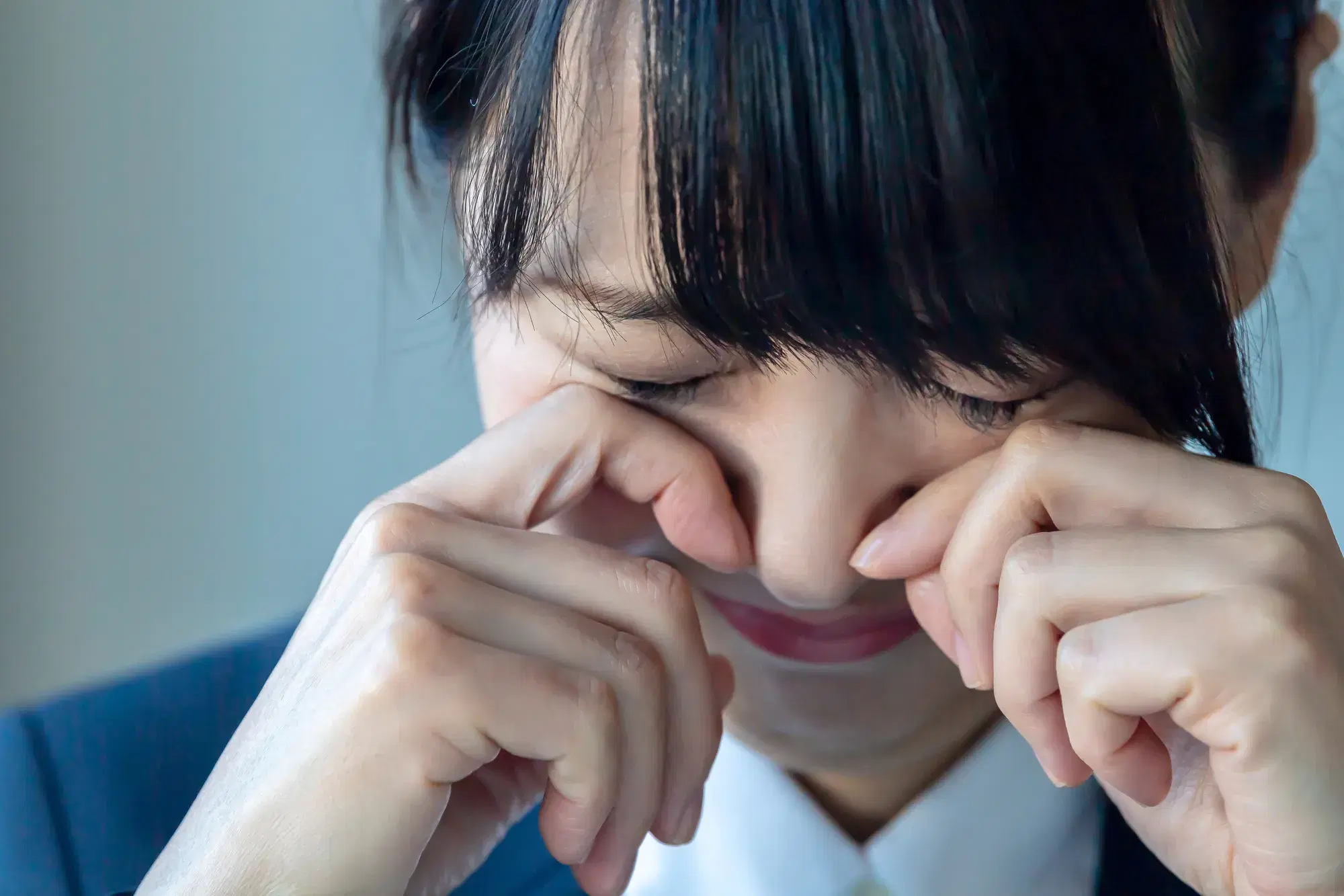 紺色のスーツを着た女性が両手で目をこすっている。