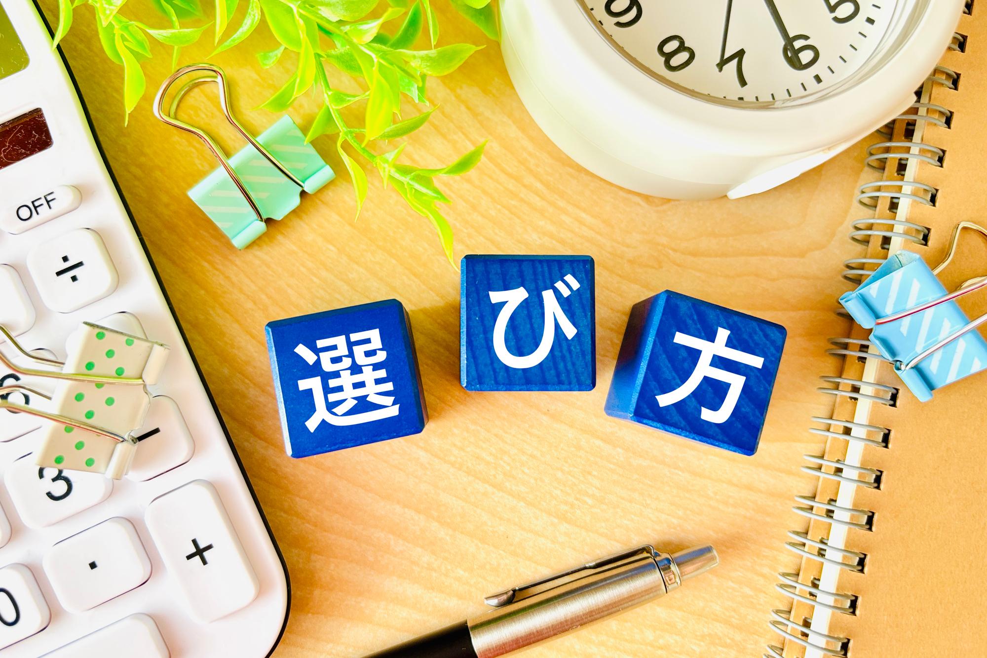 選び方と書かれた木のキューブと計算機や時計が机に散らばった様子