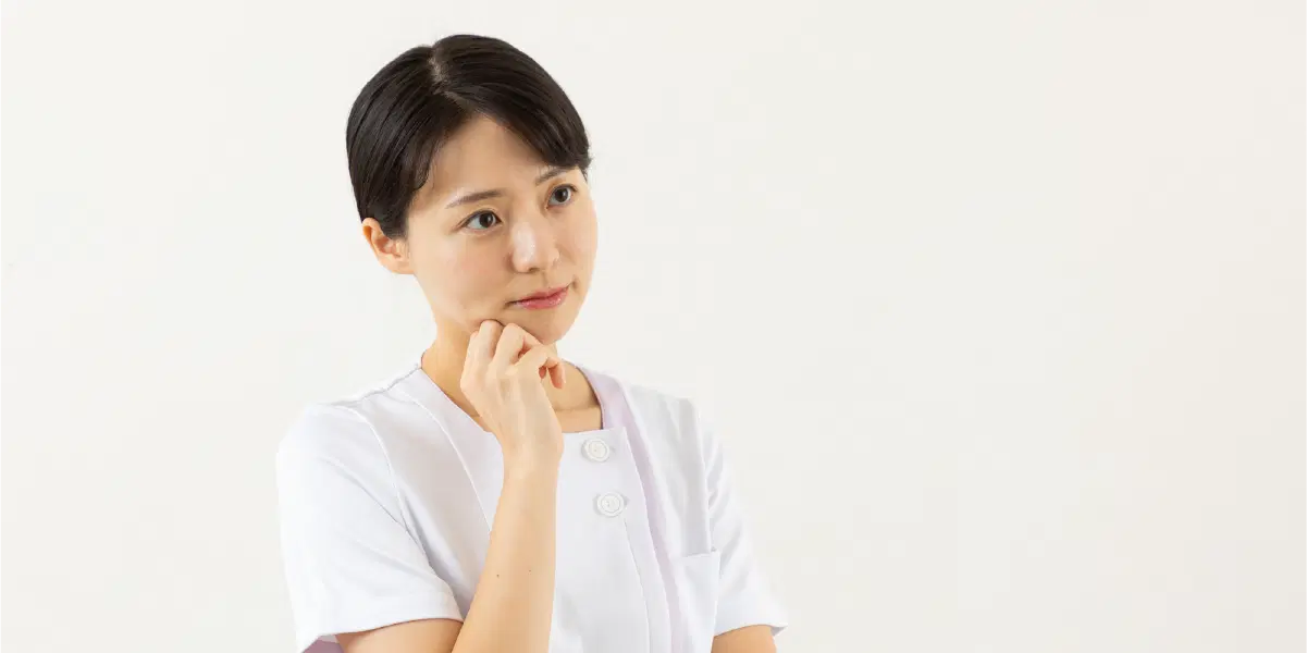 首を傾げて考える看護師服を着た女性