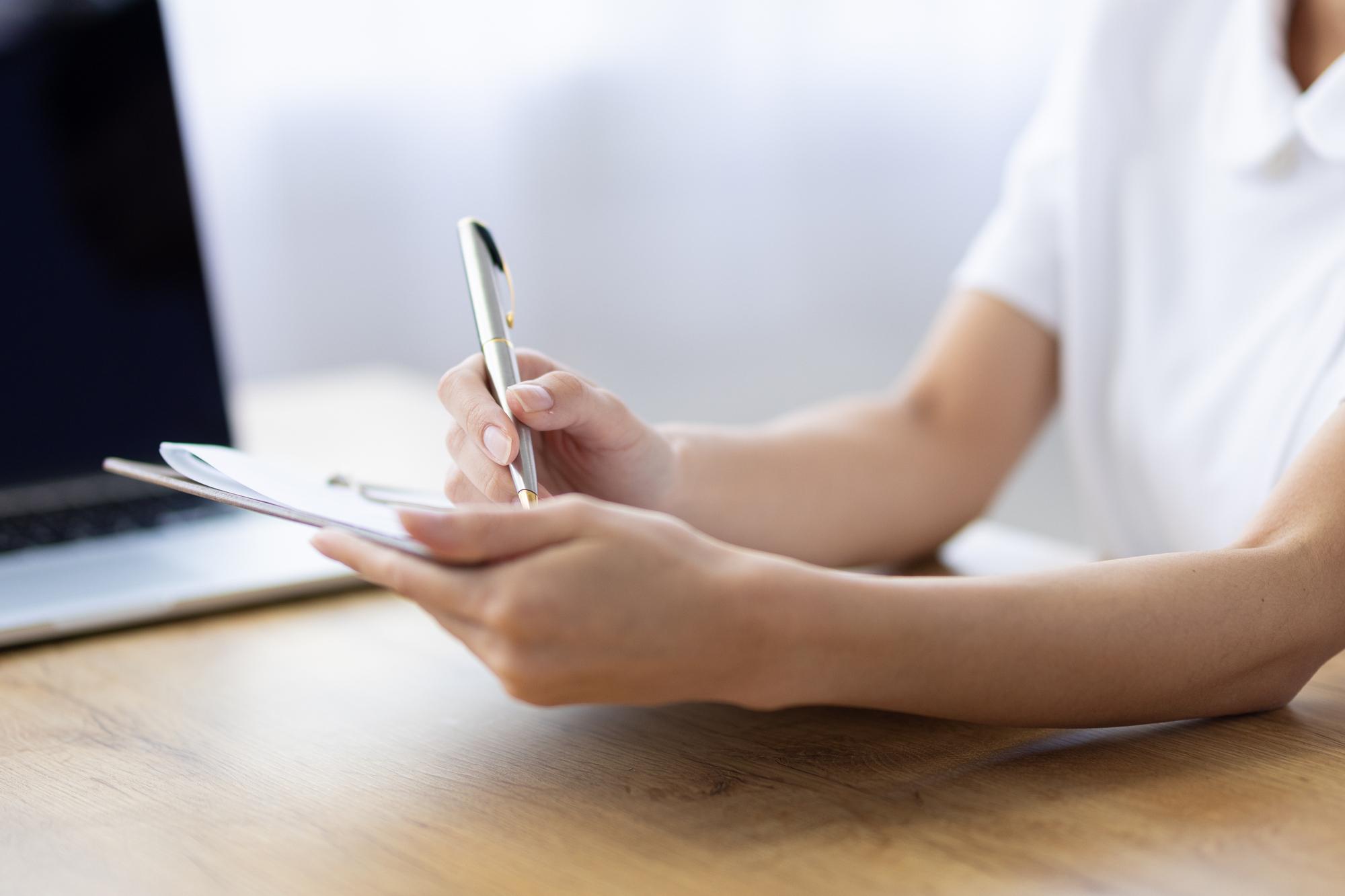 白衣を着た人がボールペンで書類に記述している