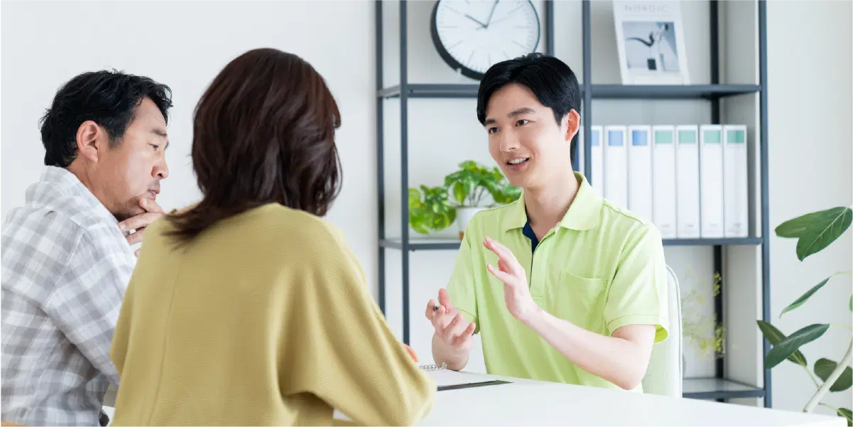 黄緑色の服を着た男性が初老の夫婦に向かって話をしている