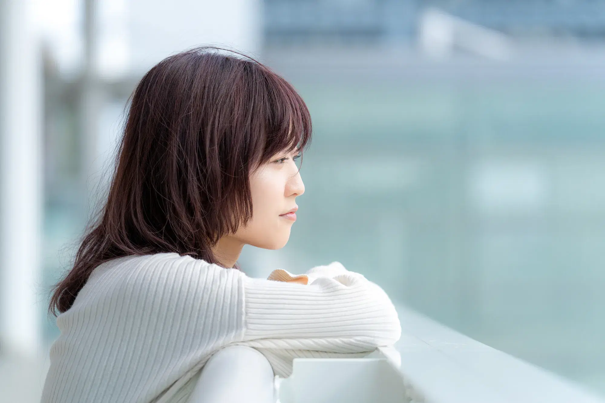 白い服を着た女性が外の手すりに体重を預けて眺めている