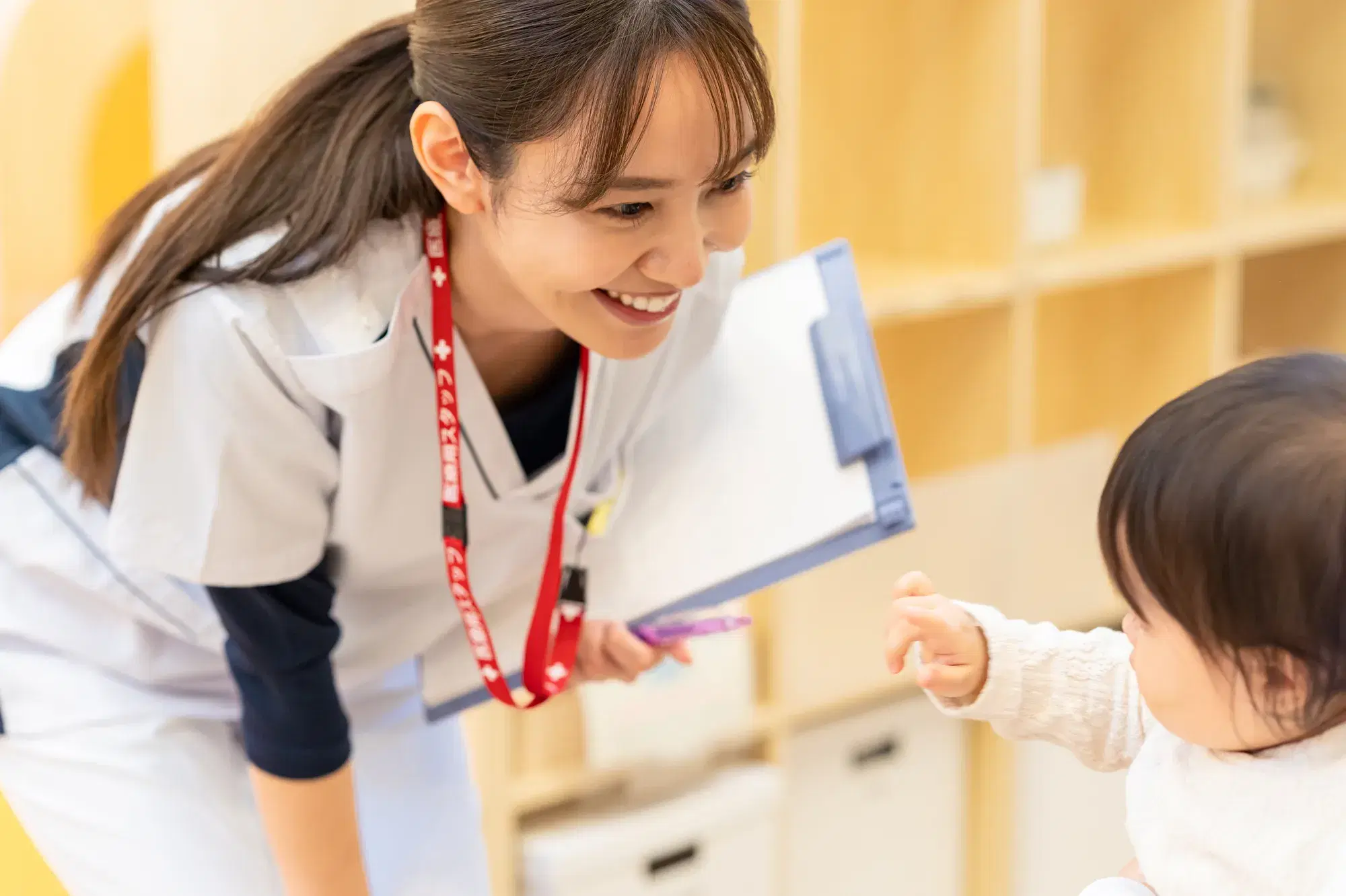 バインダーを抱えながら白い服を着た女性と子ども