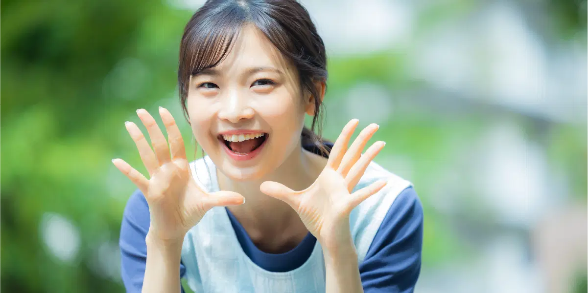 口の横に両手を広げて大きな声を出している女性