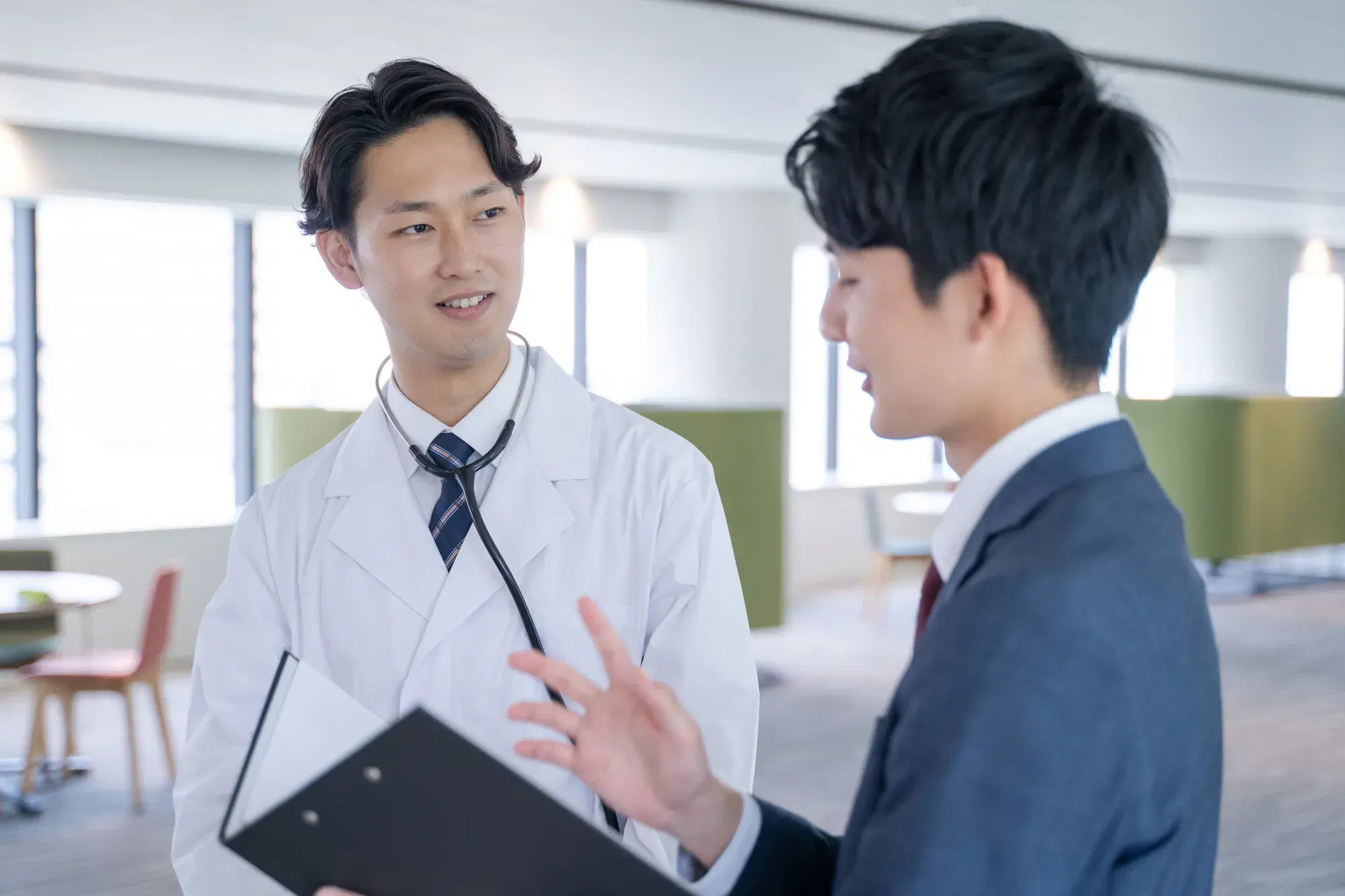 白衣を着た男性と黒いバインダーを持った紺色のスーツを着た男性