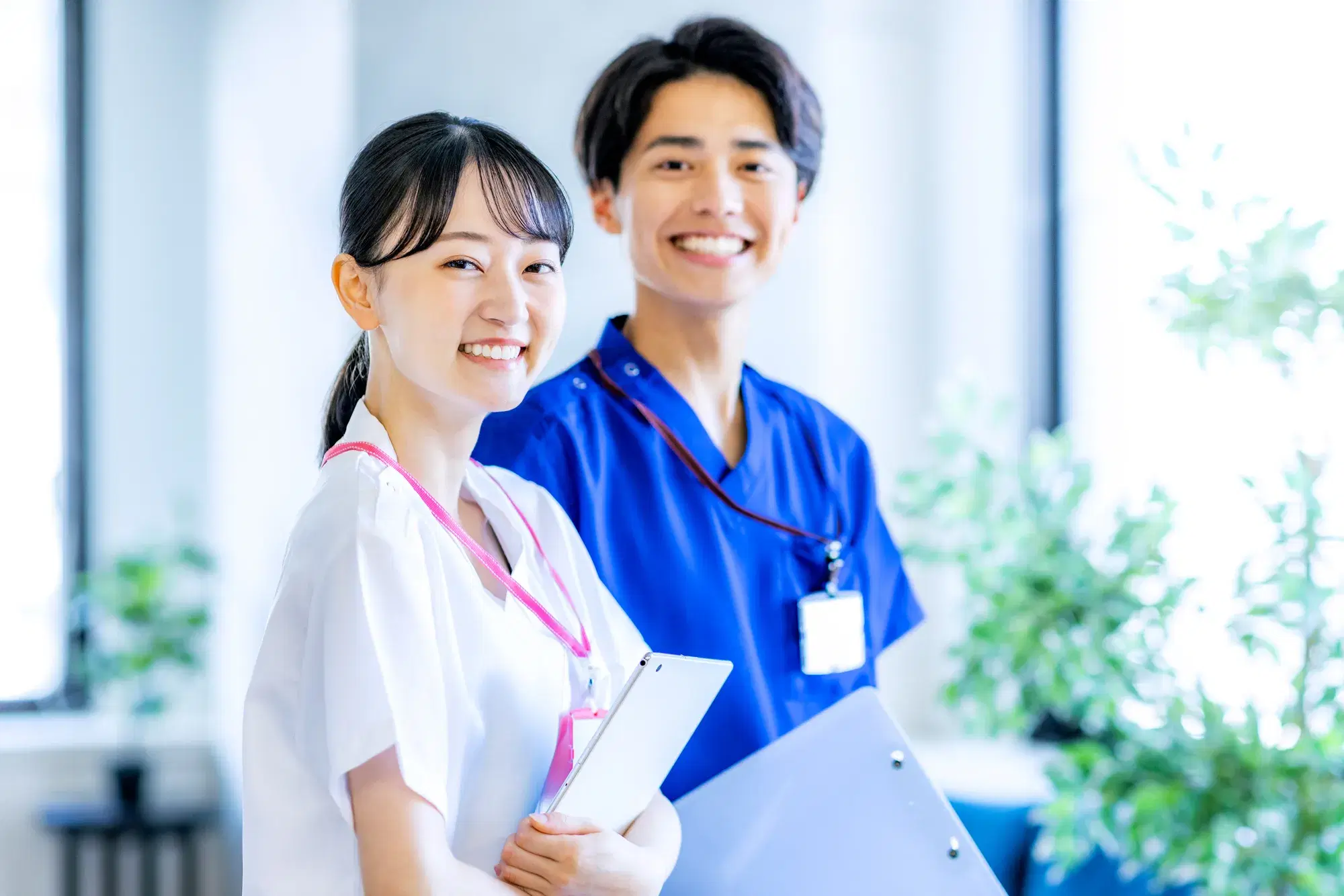 白衣を着た女性と青い医療用の服を着た男性が同じ方向を向きながら笑っている