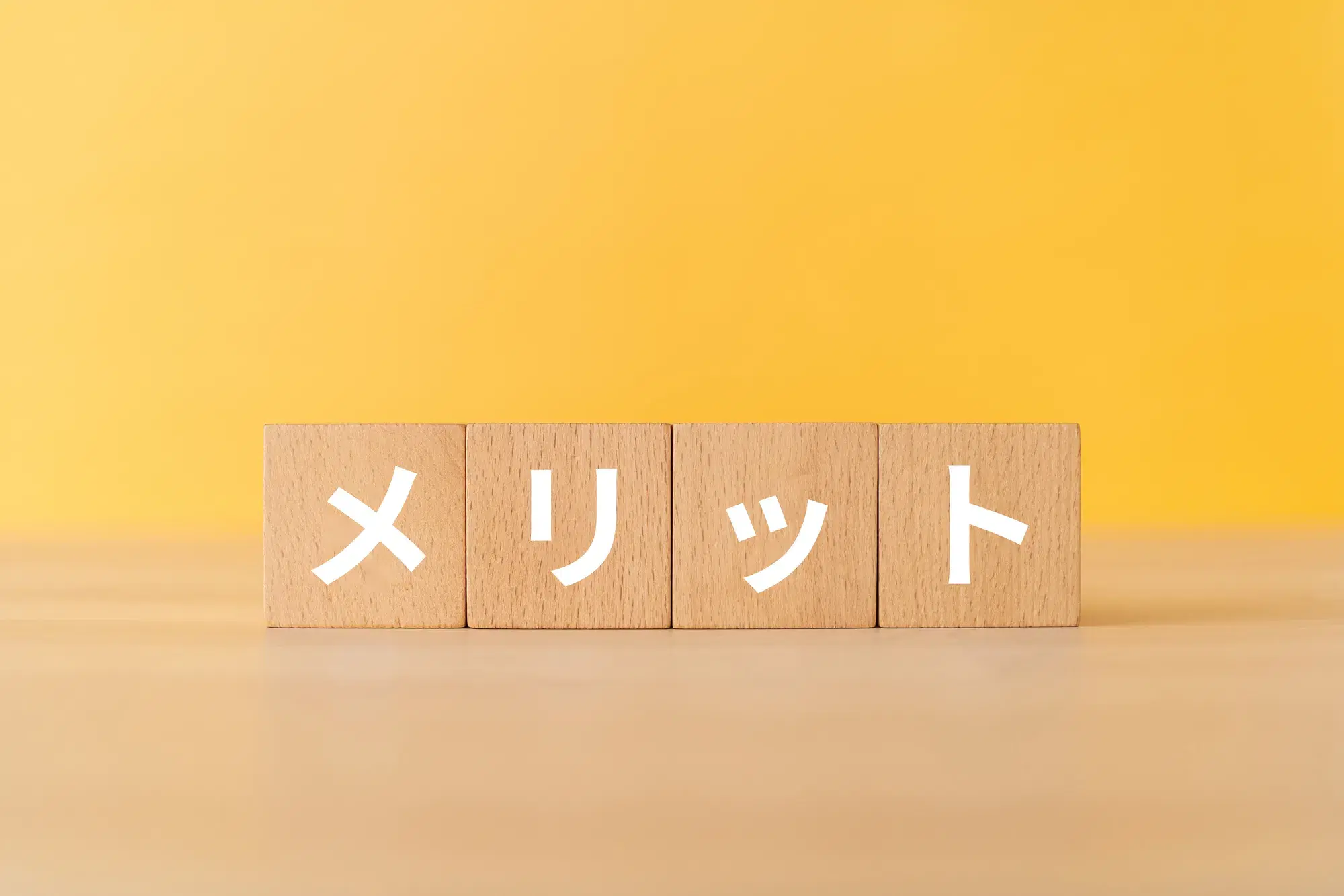 黄色い背景に木製の積み木が置いてあり、白い文字でメリットと書かれている。