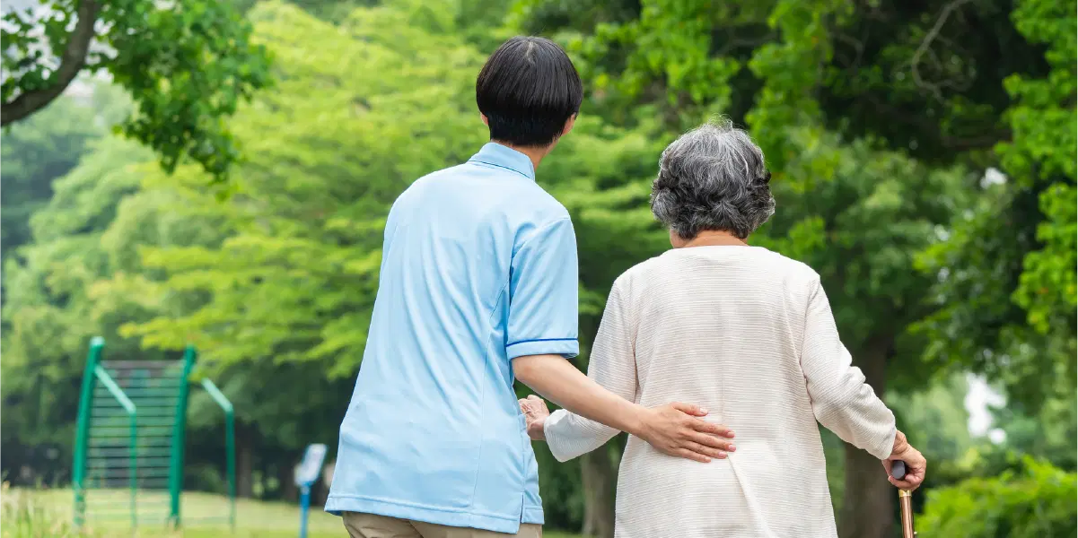 年配の女性が歩くのを水色の服を着た男性が支えている