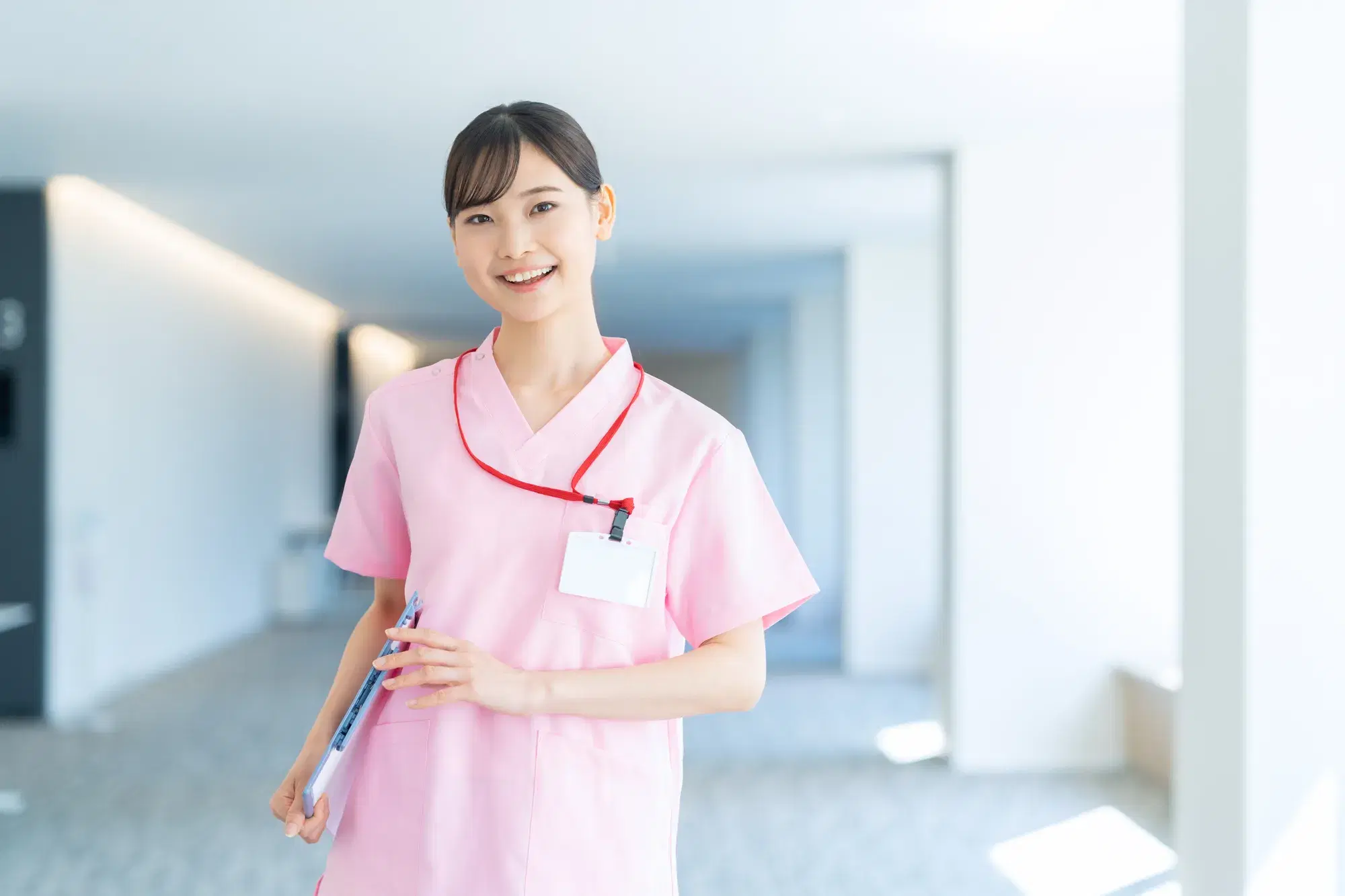 ピンクのスクラブを着た女性の医療従事者が廊下に立っている。